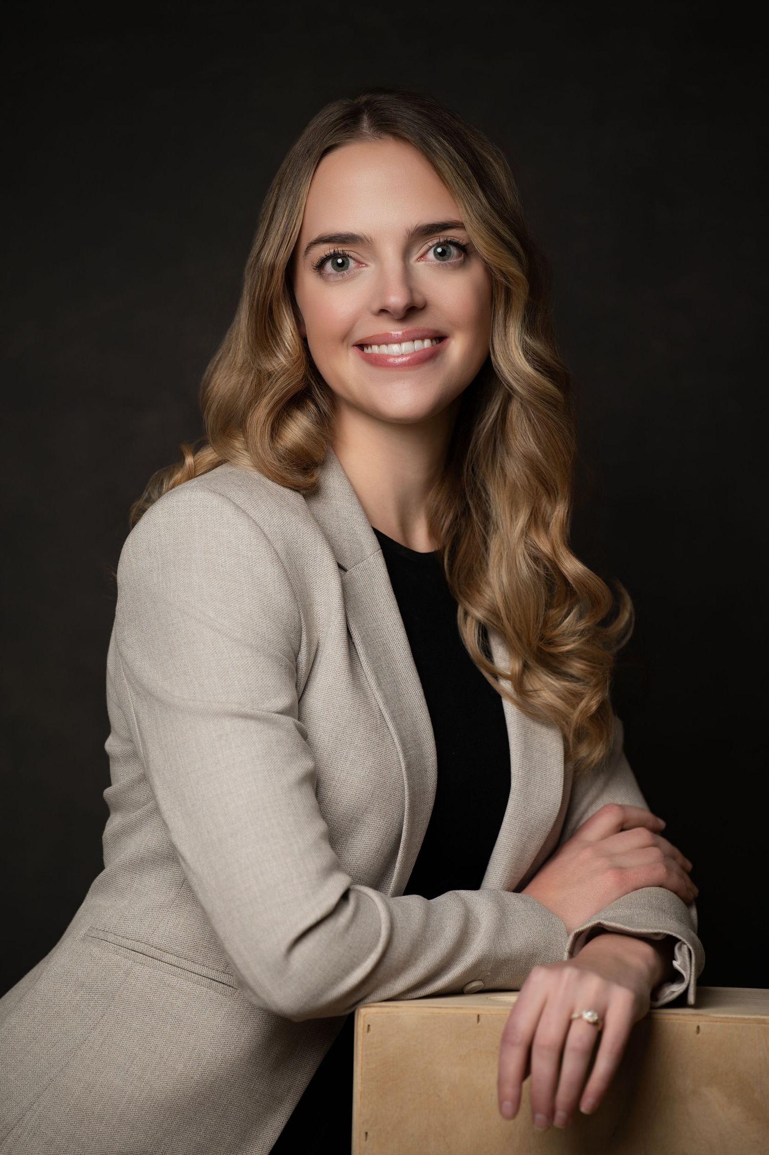 Professional portrait of person in cream blazer leaning on wooden box.
