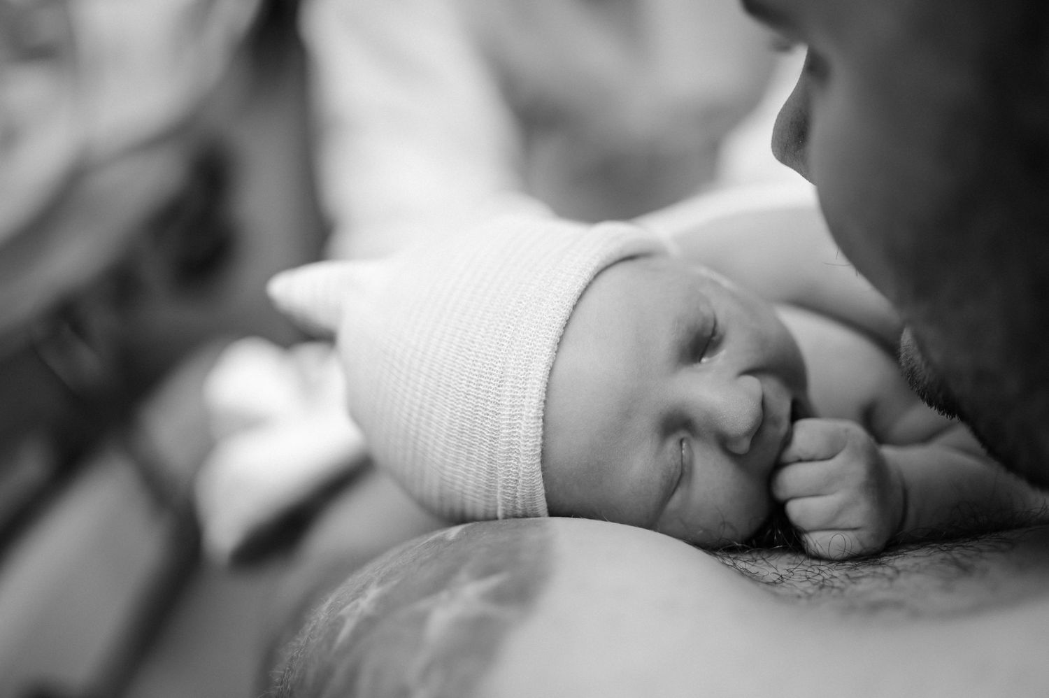 Black and white photo of newborn baby with white cap resting peacefully.