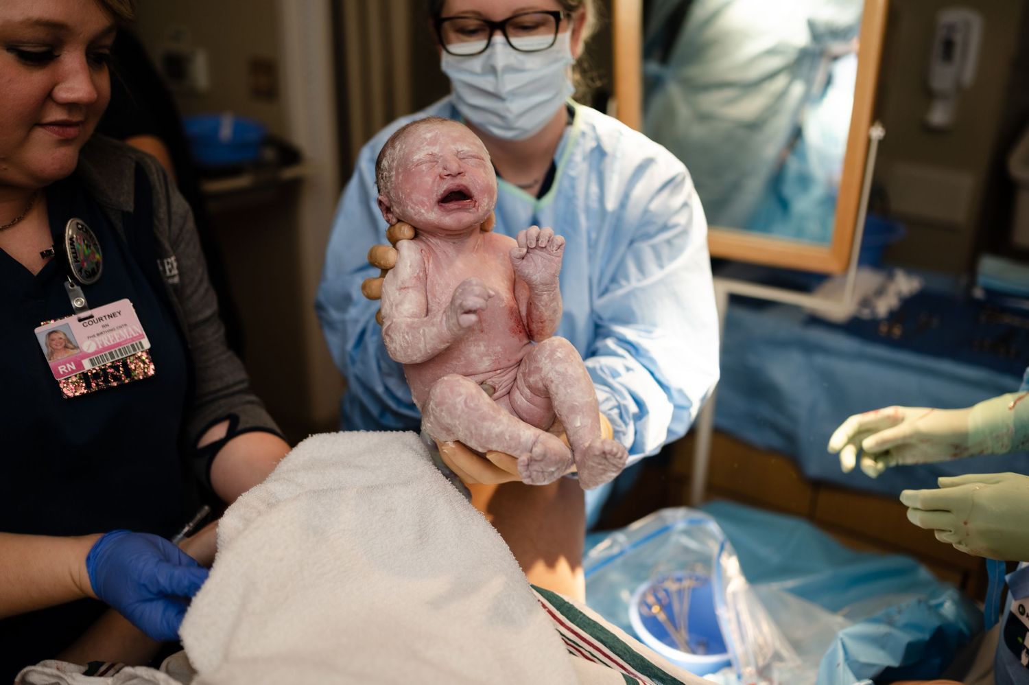 Medical team holding newborn baby in hospital room immediately after delivery.
