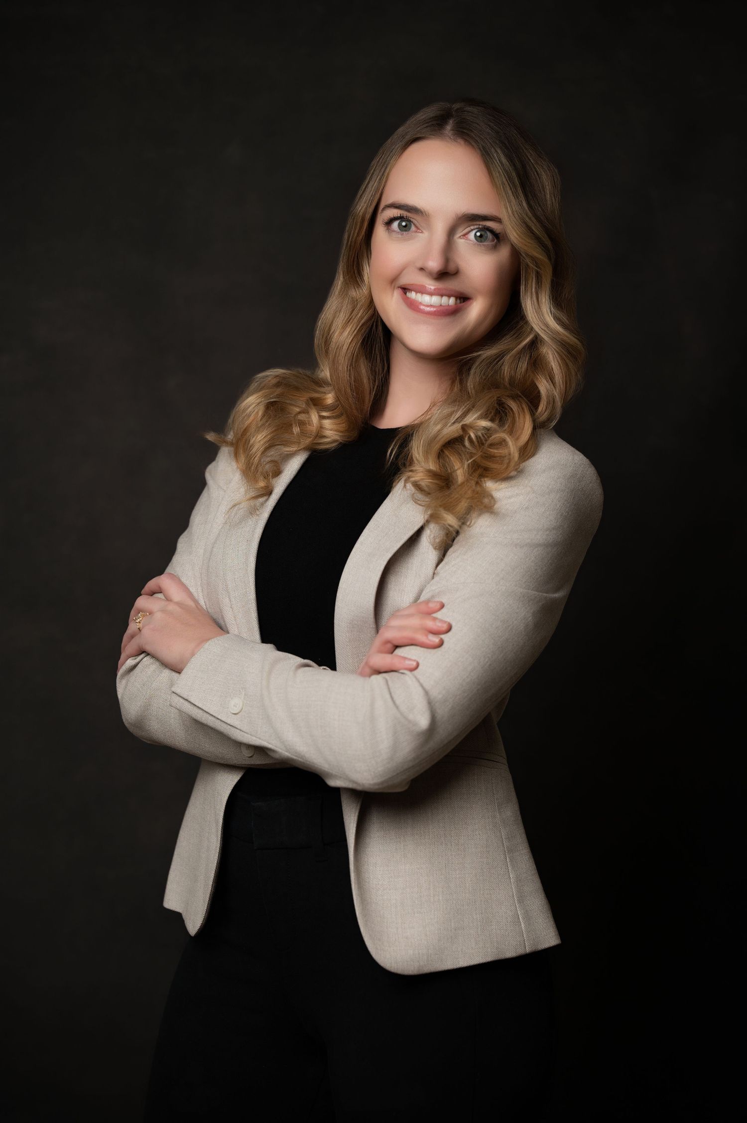 Professional studio portrait of person in cream blazer and black dress against dark background.