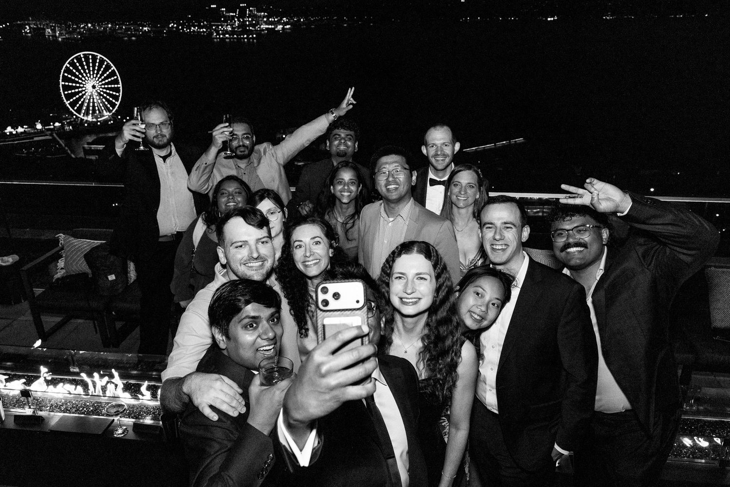 Group of friends taking a fun selfie at a rooftop party at night with a Ferris wheel in the background.