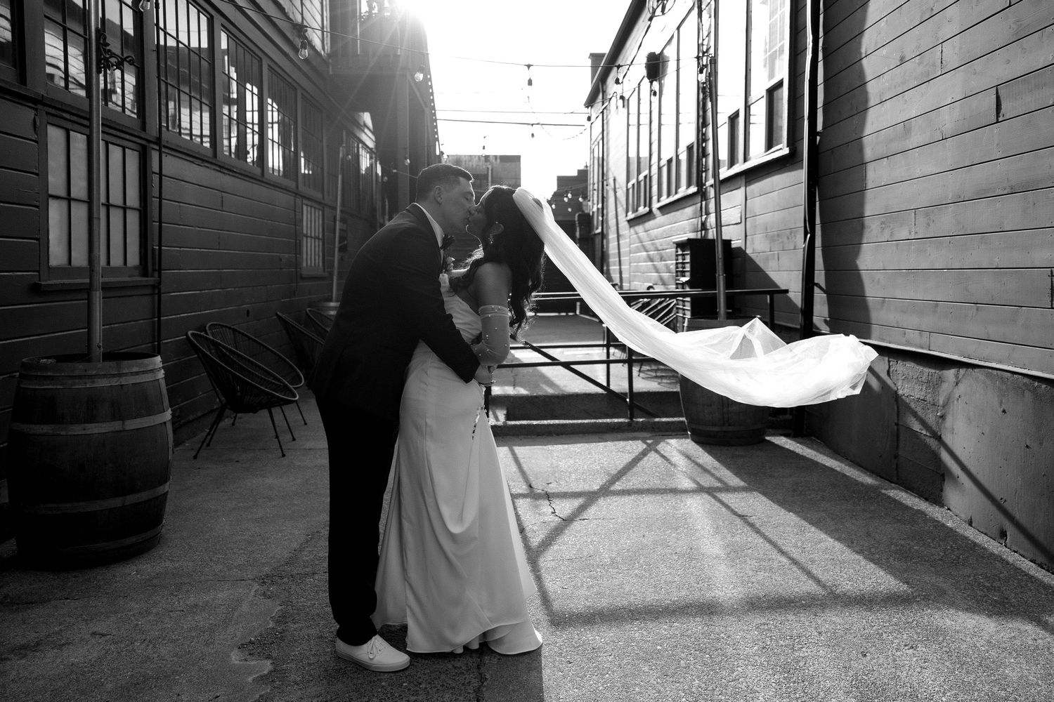 Black and white photo of a bride and groom sharing a kiss outdoors at Within SoDo, her veil flowing in the wind.