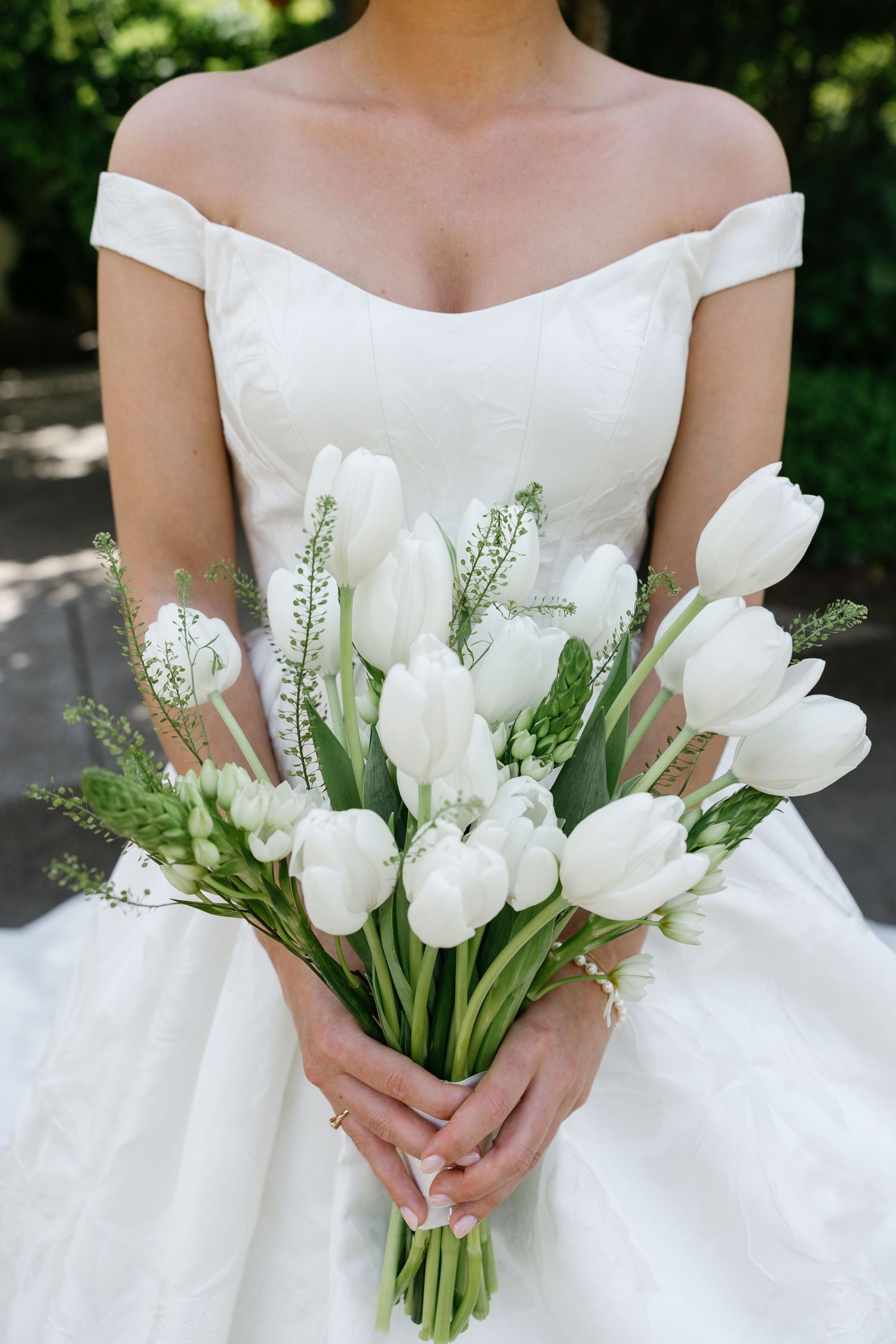 A white tulip and lily of the valley bridal bouquet shown from different angles against a wedding dress.