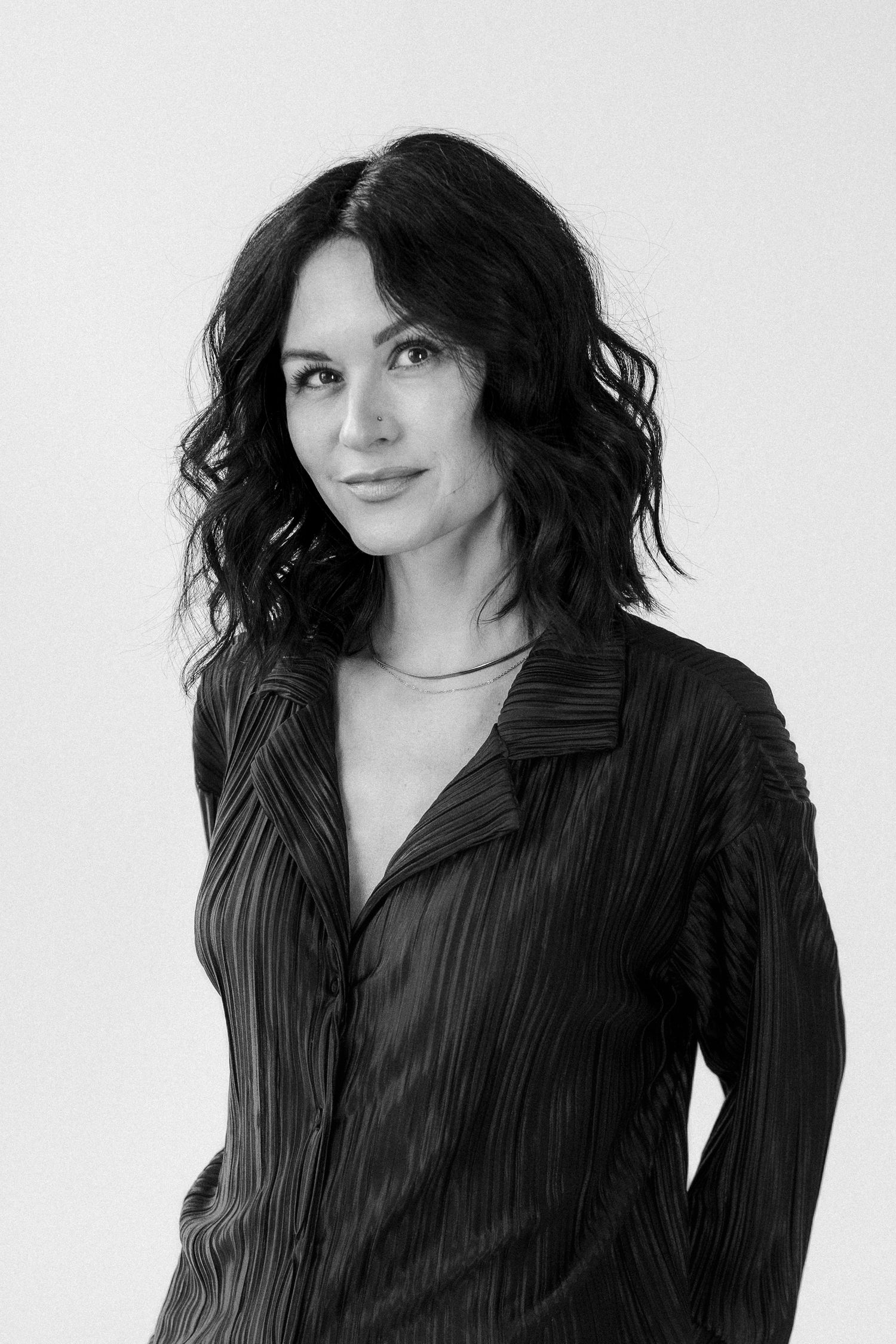 Black and white portrait of Carley Azorit wearing a silk button-up shirt against a light background.