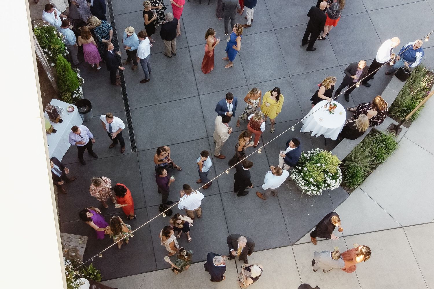 Aerial view of people gathered on a gray concrete plaza with shadows casting geometric patterns across the space.