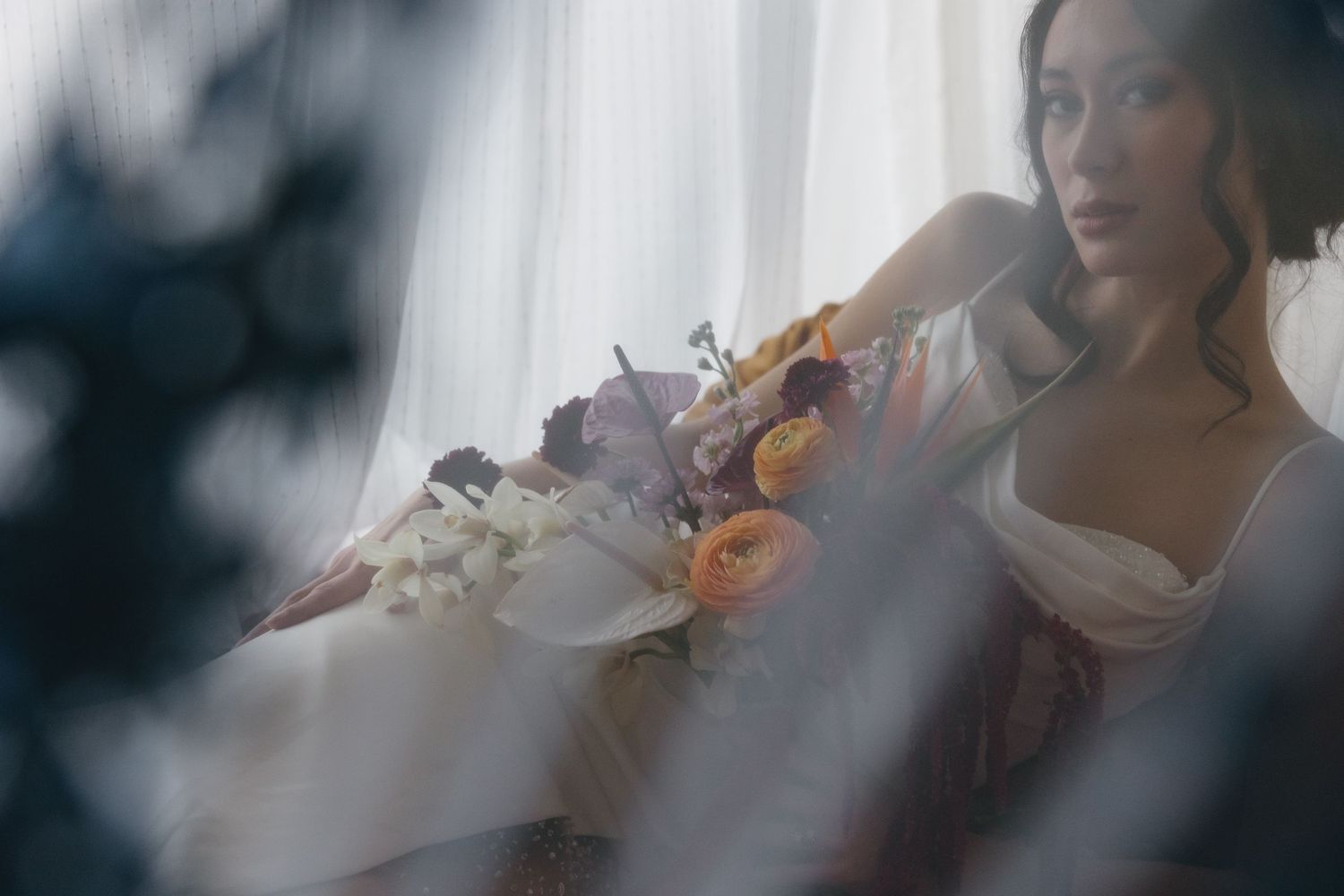 A bride holds a vibrant bouquet against a soft, dreamy background with blurred edges.