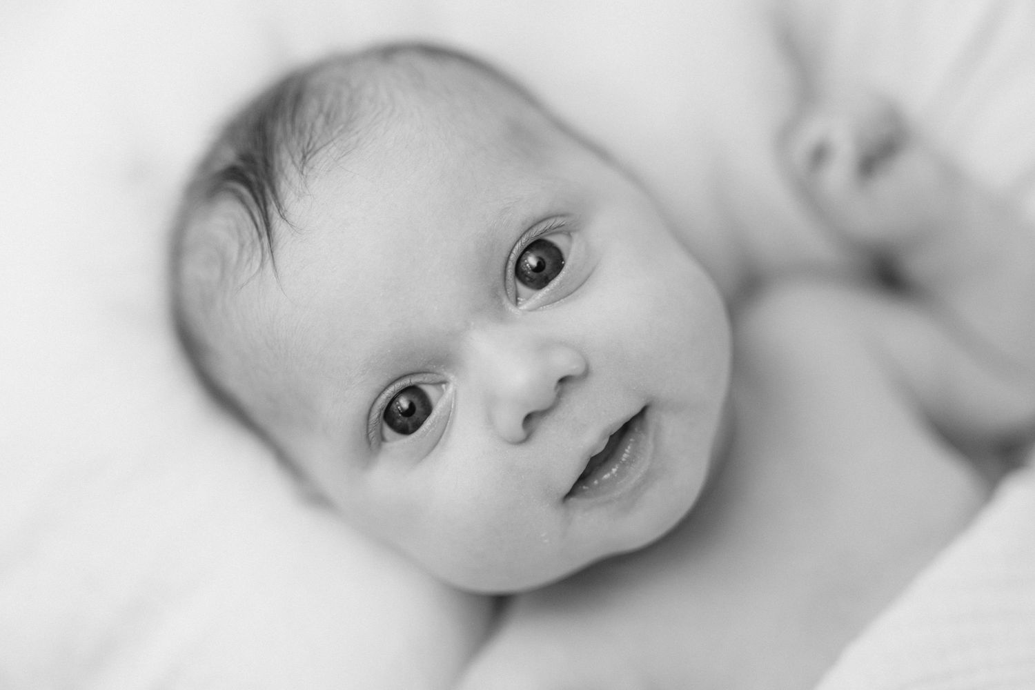 Black and white close-up portrait of a newborn baby with bright eyes and a gentle smile.