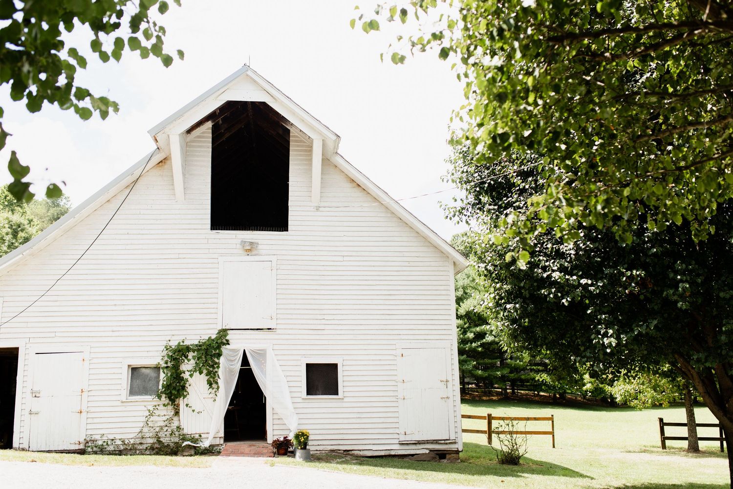 Charming white barn venue surrounded by lush green trees on a sunny summer day.