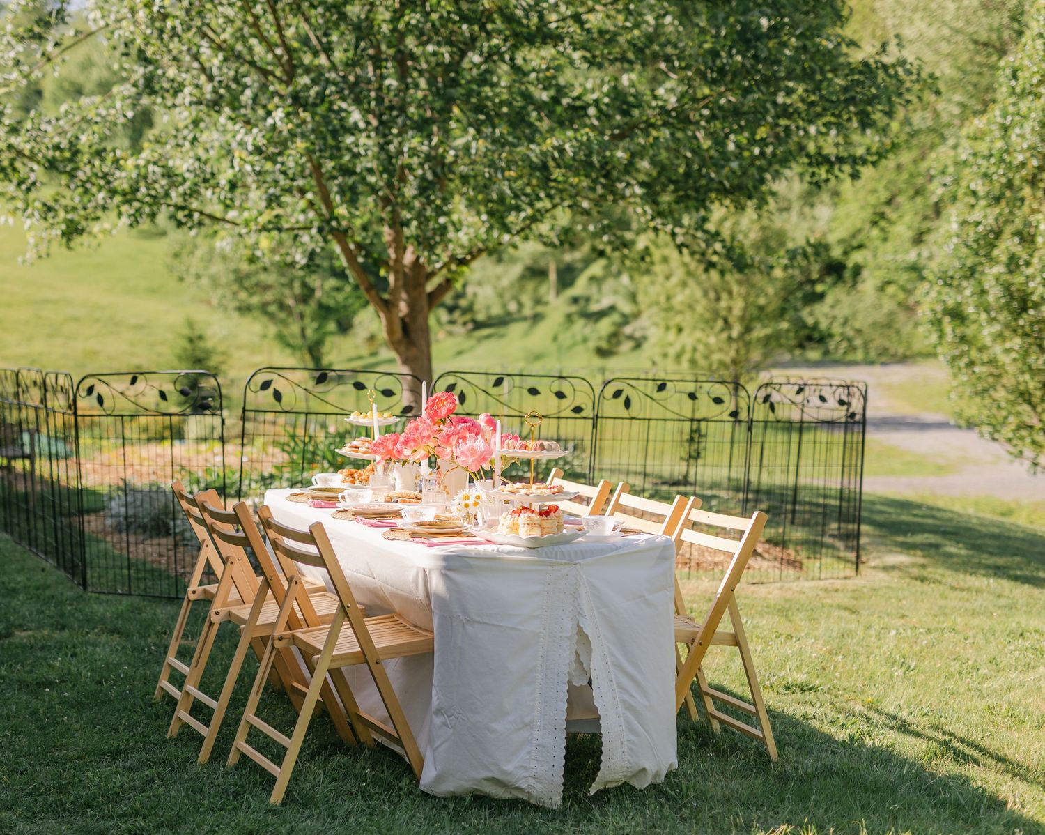 Outdoor garden dining table set with floral centerpiece under a tree with wooden folding chairs.