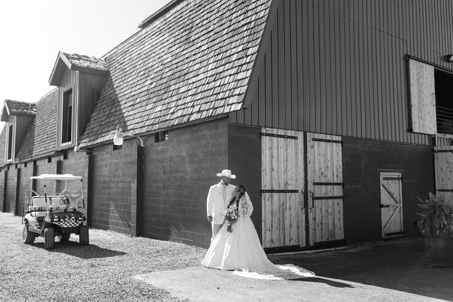 Bride and groom share a romantic moment outside a rustic black barn with a golf cart nearby.