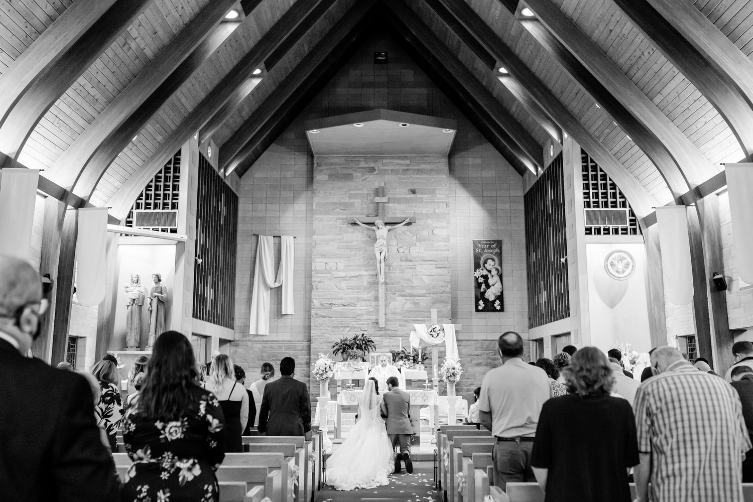 Black and white photo of a wedding ceremony inside a Catholic church with guests filling the pews.