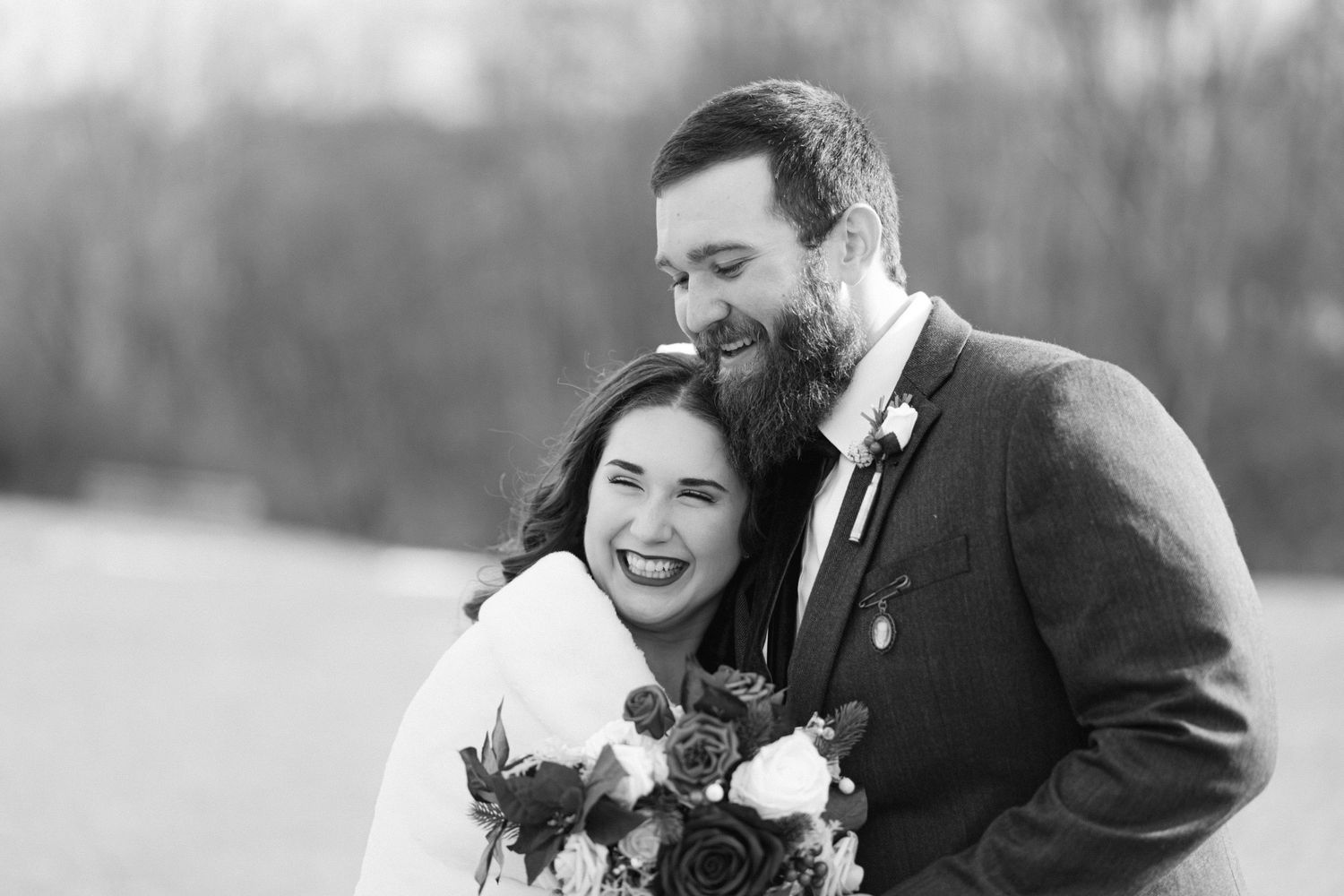 Black and white photo of smiling bride and groom embracing outdoors on their wedding day.