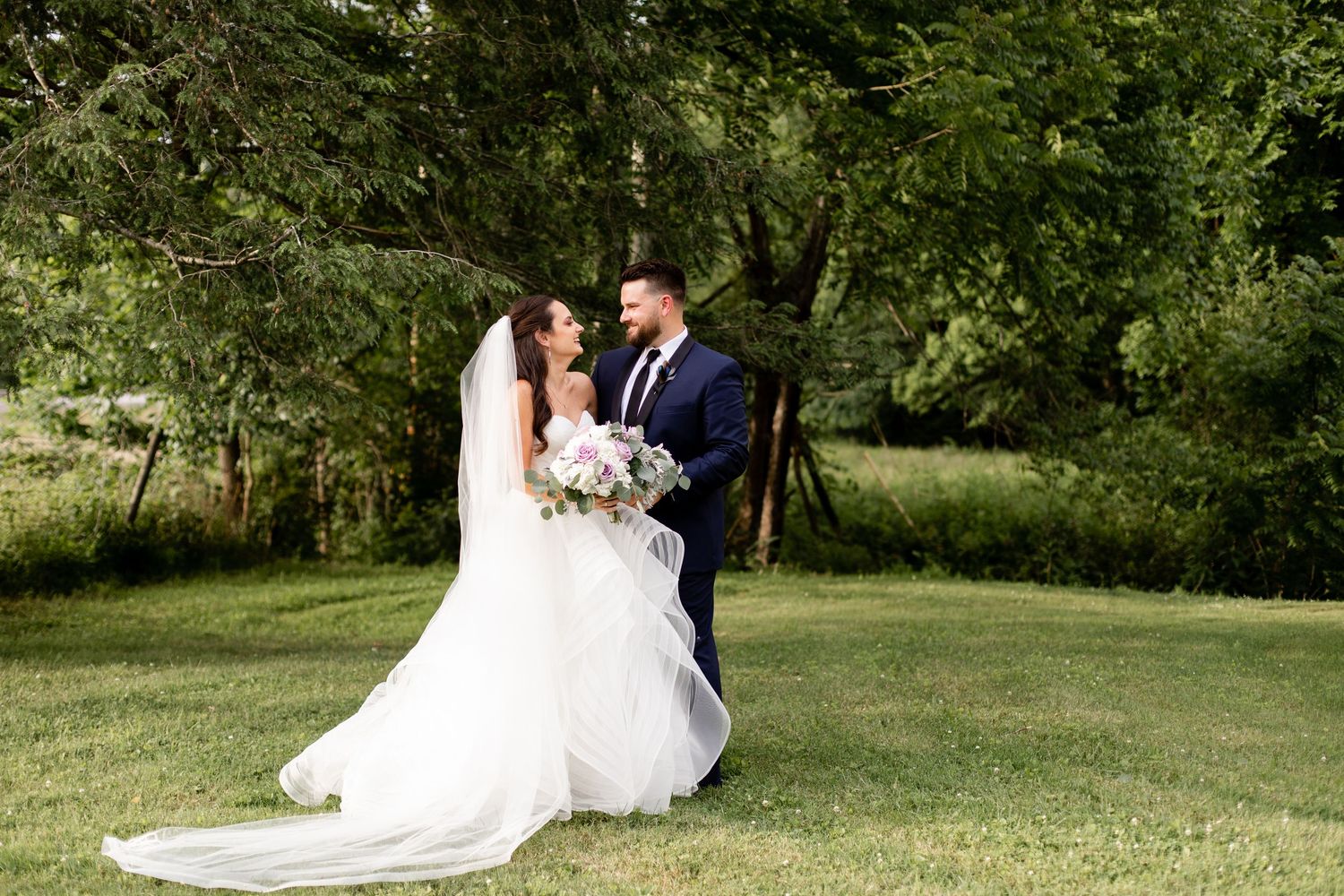 Bride and groom sharing romantic moment in lush green garden, bride in flowing cathedral veil.