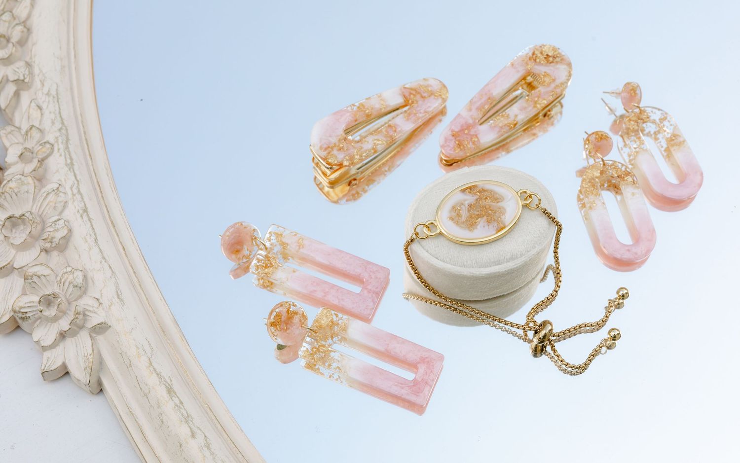 Pink resin hair clips, earrings, and bracelet jewelry set displayed on mirror surface with gold accents.