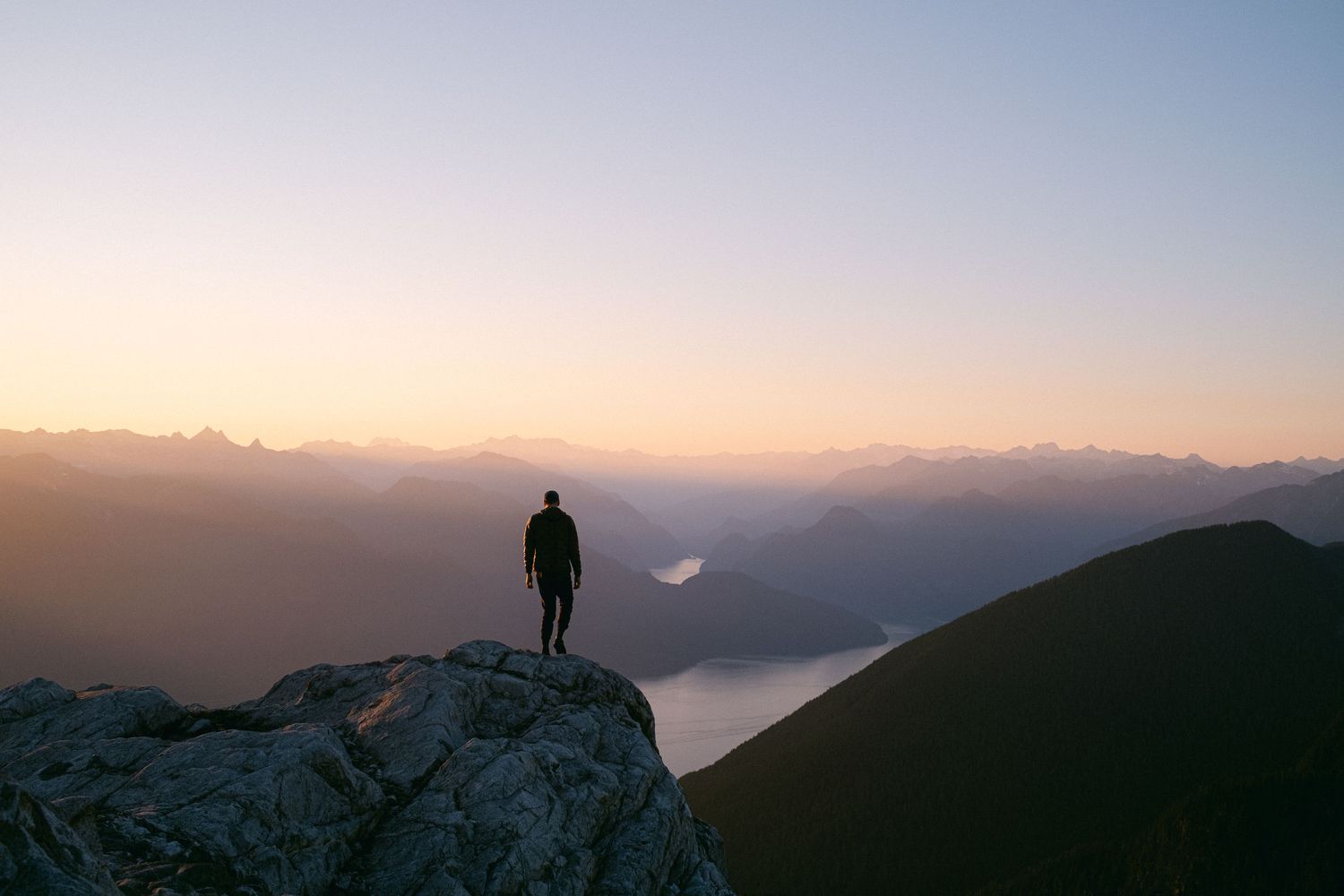 Silhouette of person standing on mountain peak overlooking misty valley at sunrise.