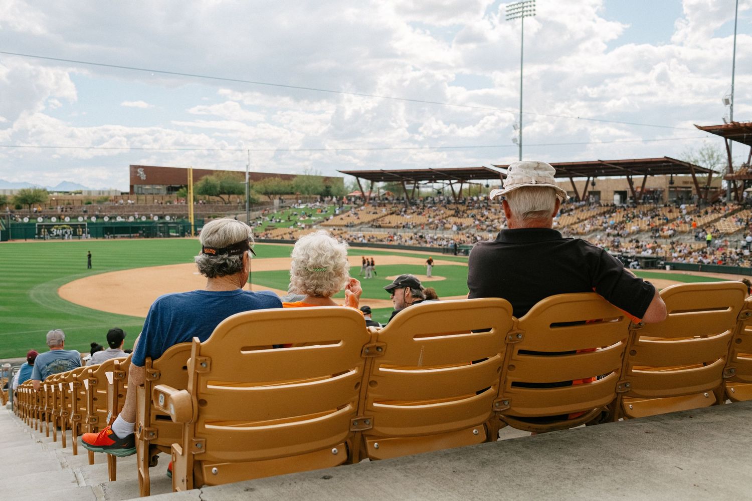 Three spectators watching baseball game from stadium seats on sunny afternoon.