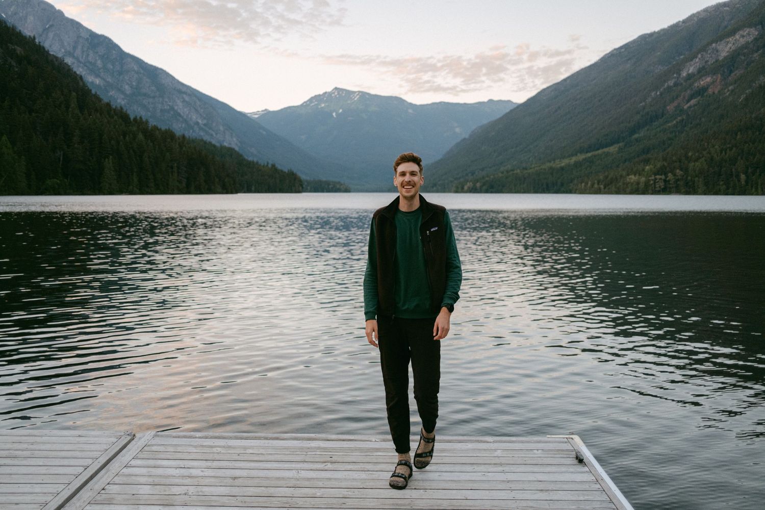 Tranquil mountain lake scene with wooden dock and reflective water at dusk.