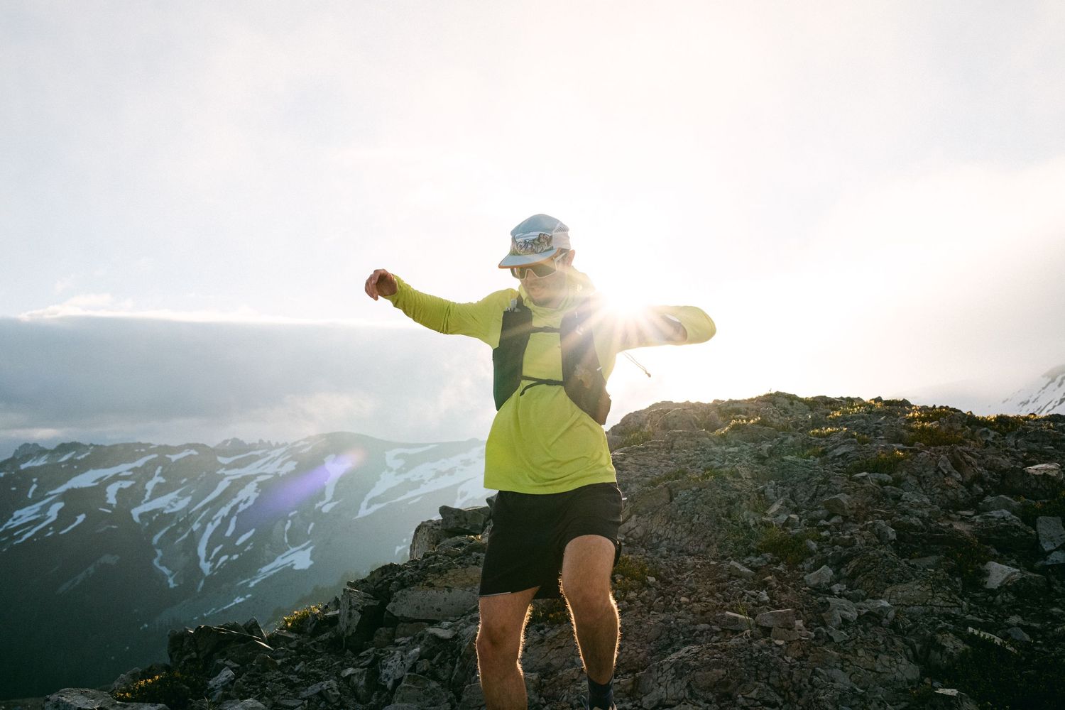 Hiker celebrating on rocky mountain peak with arms outstretched in morning light.
