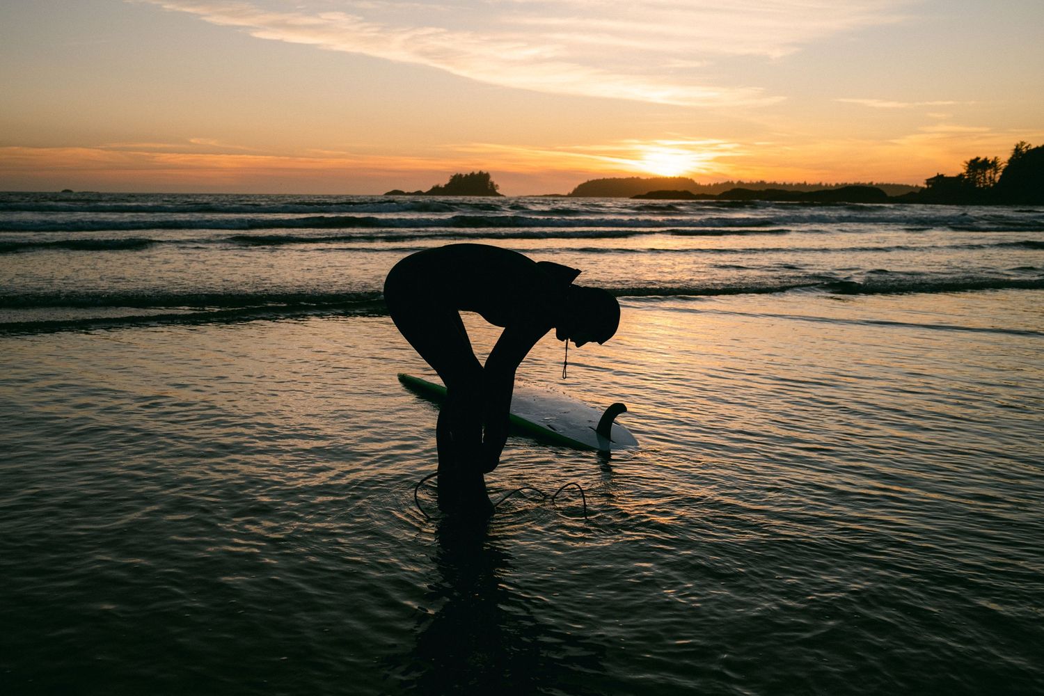 Silhouette bending over in shallow ocean water during golden sunset.