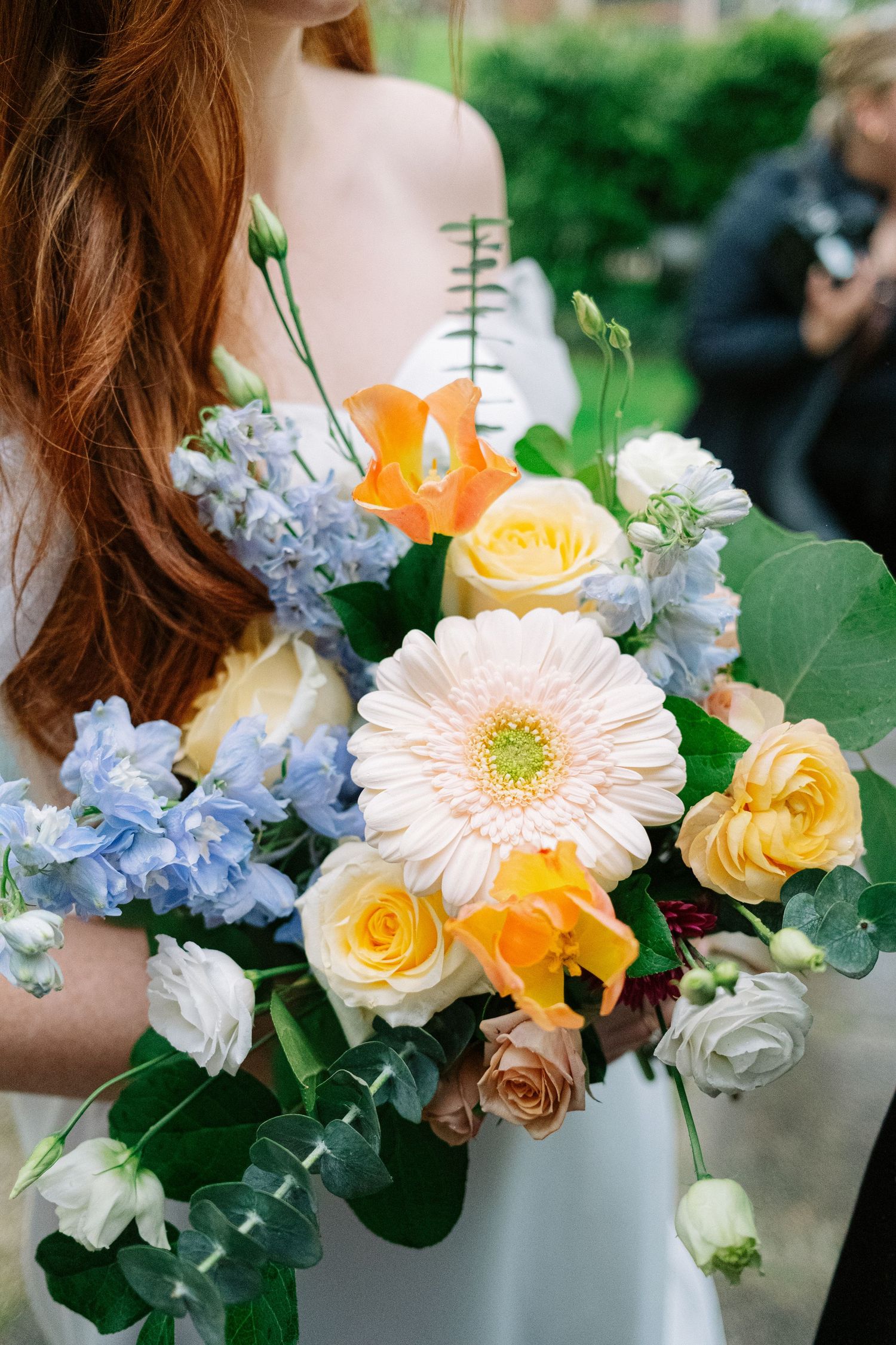 A vibrant bouquet featuring pink gerbera daisies, yellow roses, blue hydrangeas, and orange flowers with green foliage.