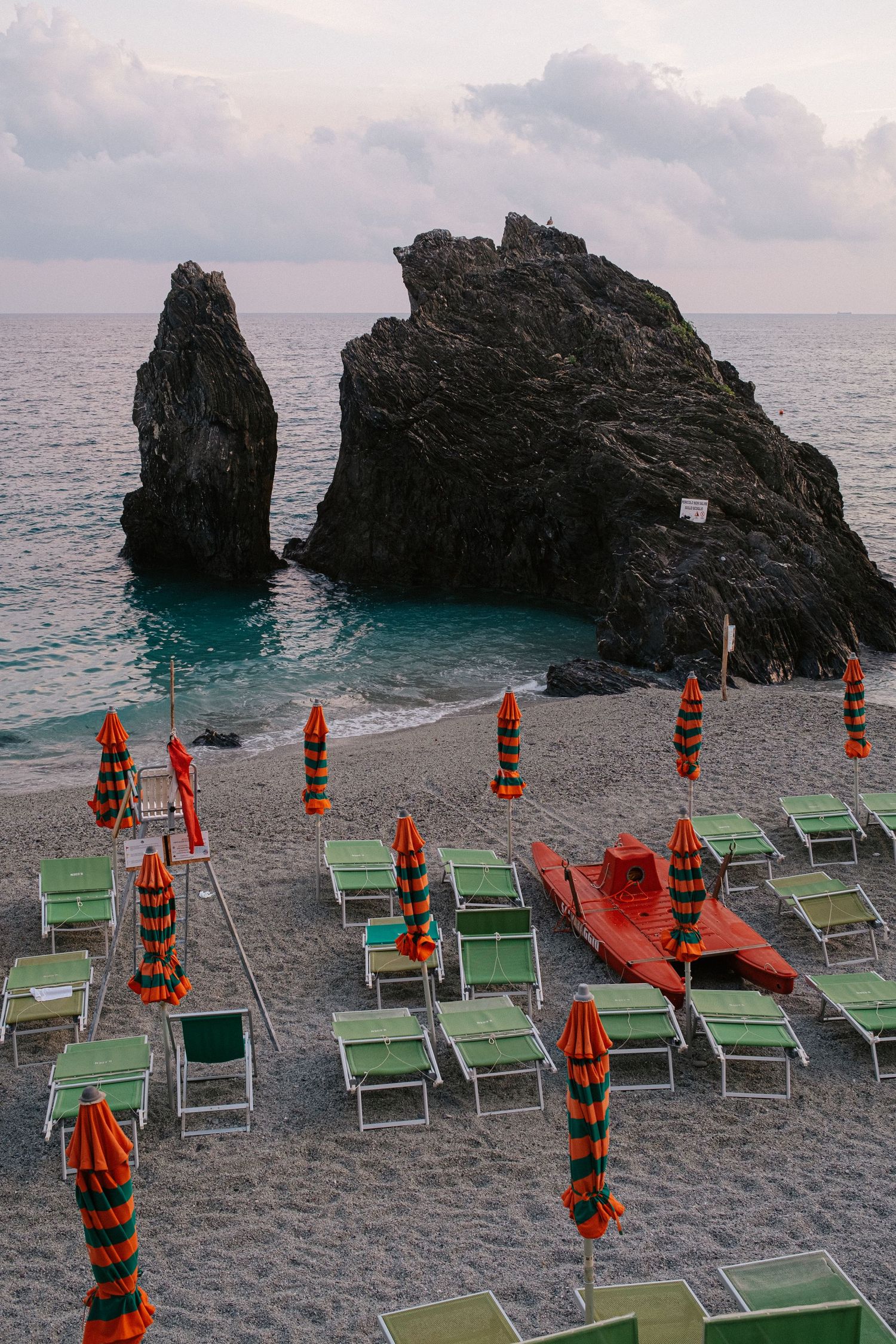 Beach umbrellas and lounge chairs arranged near dramatic rock formations on Mediterranean coastline.