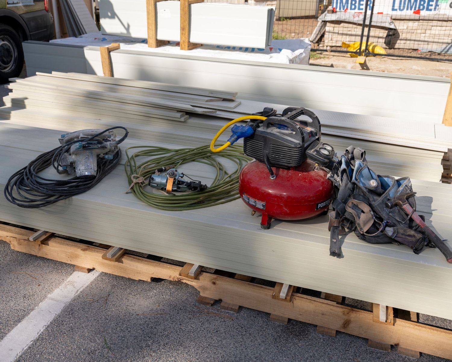 Air compressor, nail guns, extension cords, and hoses on lumber at a construction supply yard.