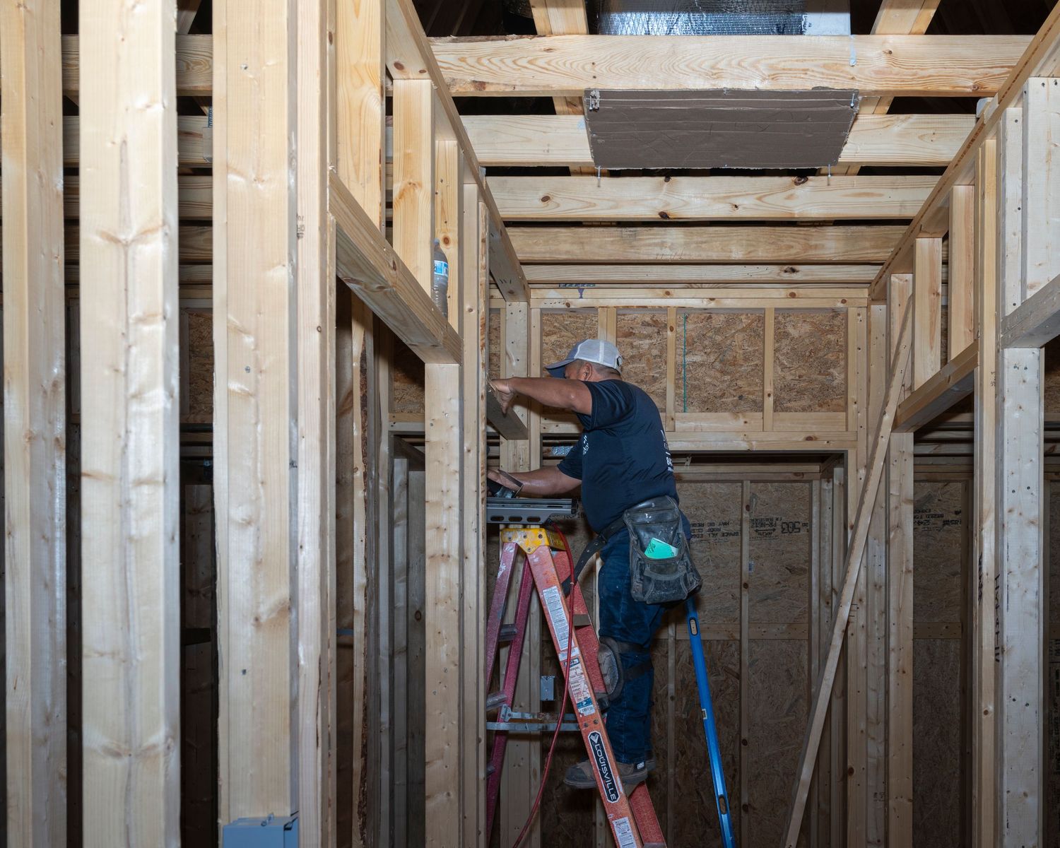 Construction worker on ladder framing interior walls of new home build with wooden studs.