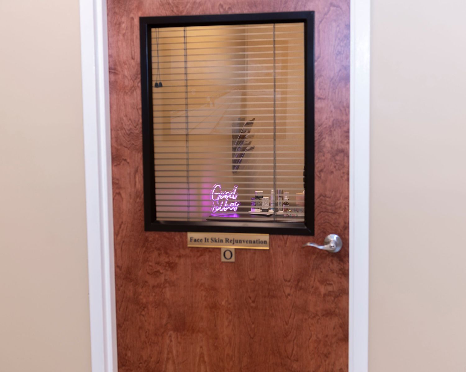 Wooden office door with frosted glass window, blinds, neon sign, and gold nameplate in a professional setting.