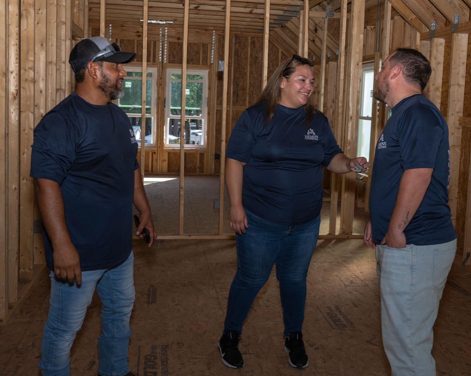 Three colleagues in matching navy shirts discuss plans inside a wood-framed building under construction.