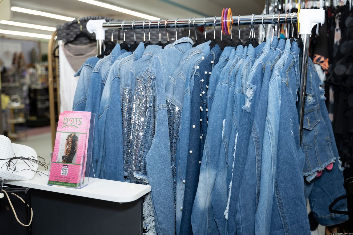 Rack of denim jackets with sequin and pearl embellishments displayed in a retail clothing store.