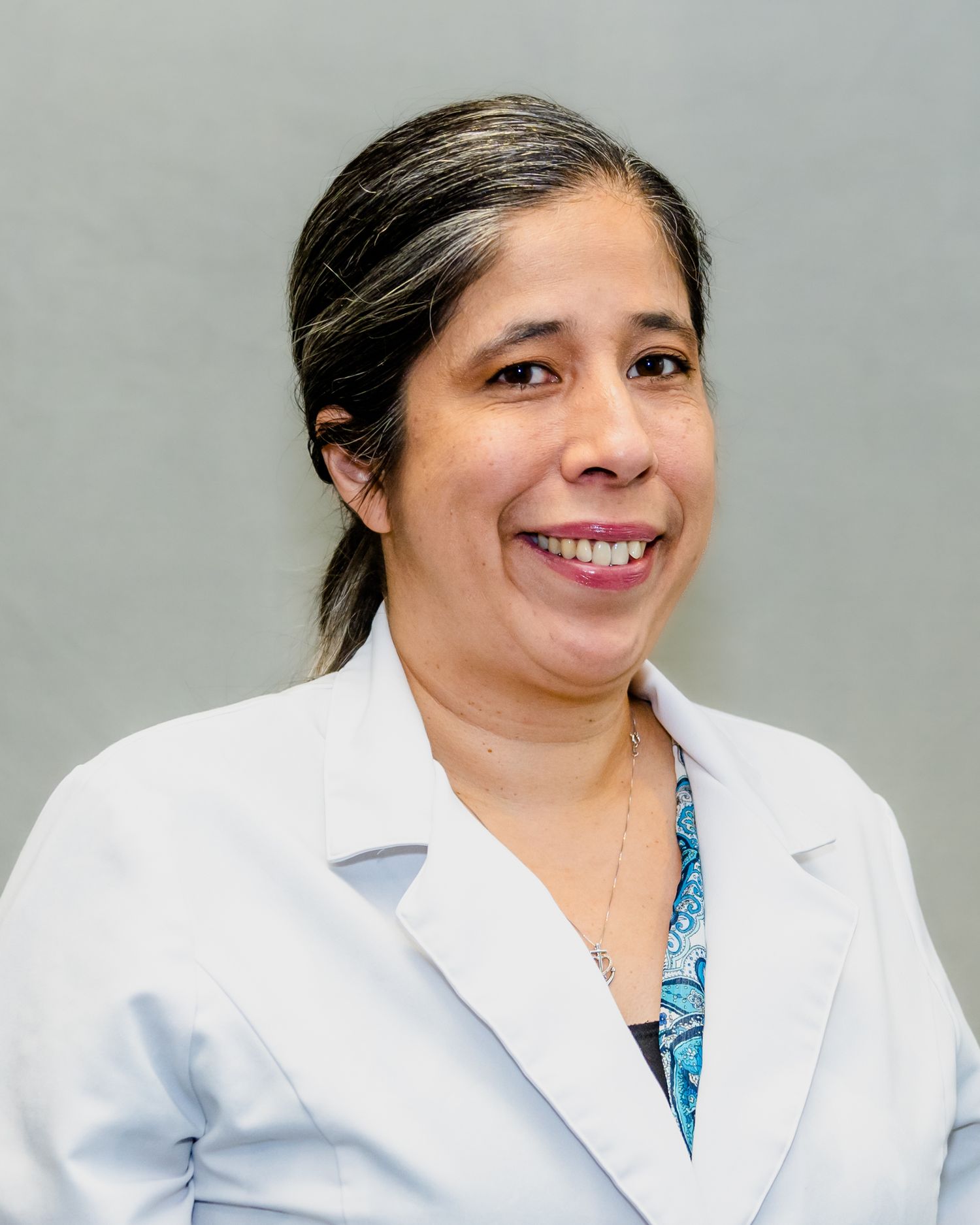 Female doctor in white lab coat smiling professionally against a gray background.