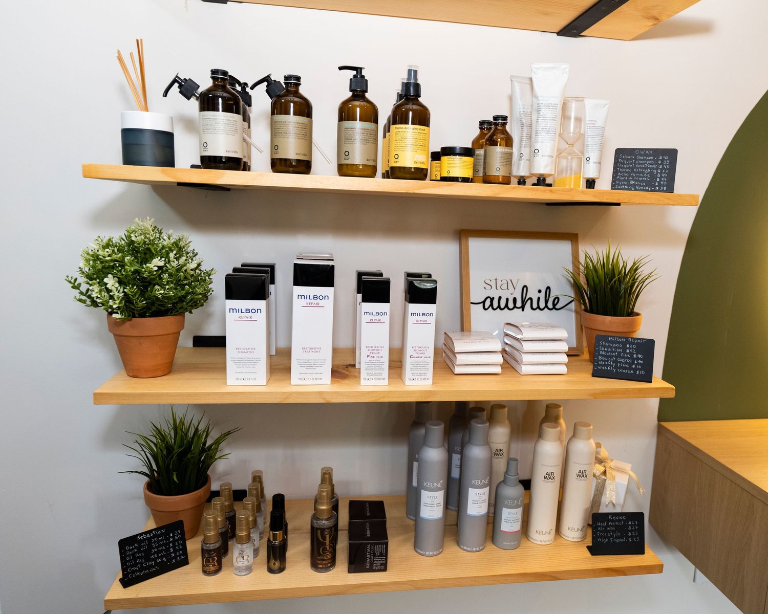 Wooden shelves displaying hair care products, amber bottles, white boxes, and small potted plants in a modern salon.