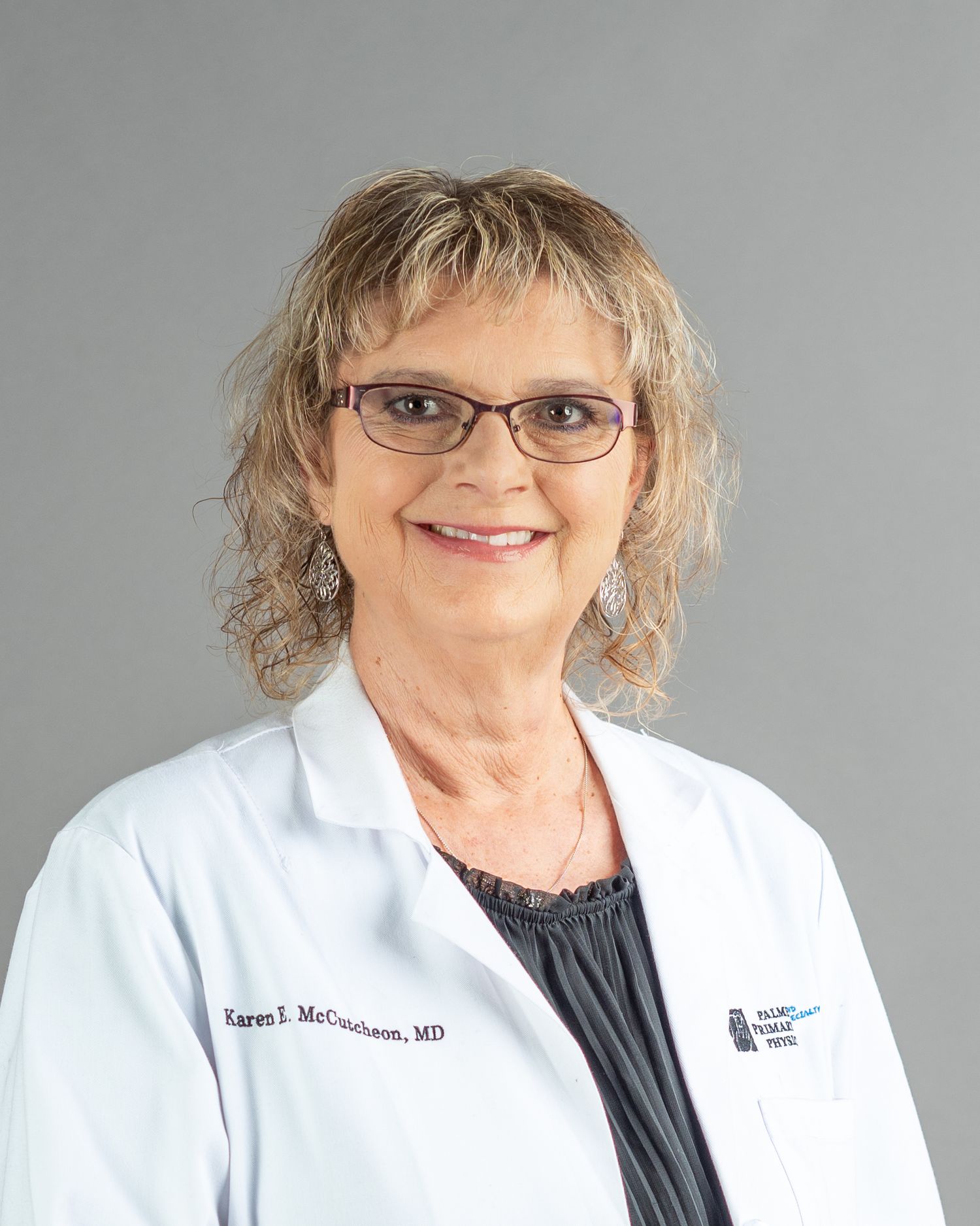 Dr. Karen J. McCutcheon, MD, smiling in a white medical coat, wearing glasses, with curly blonde hair.