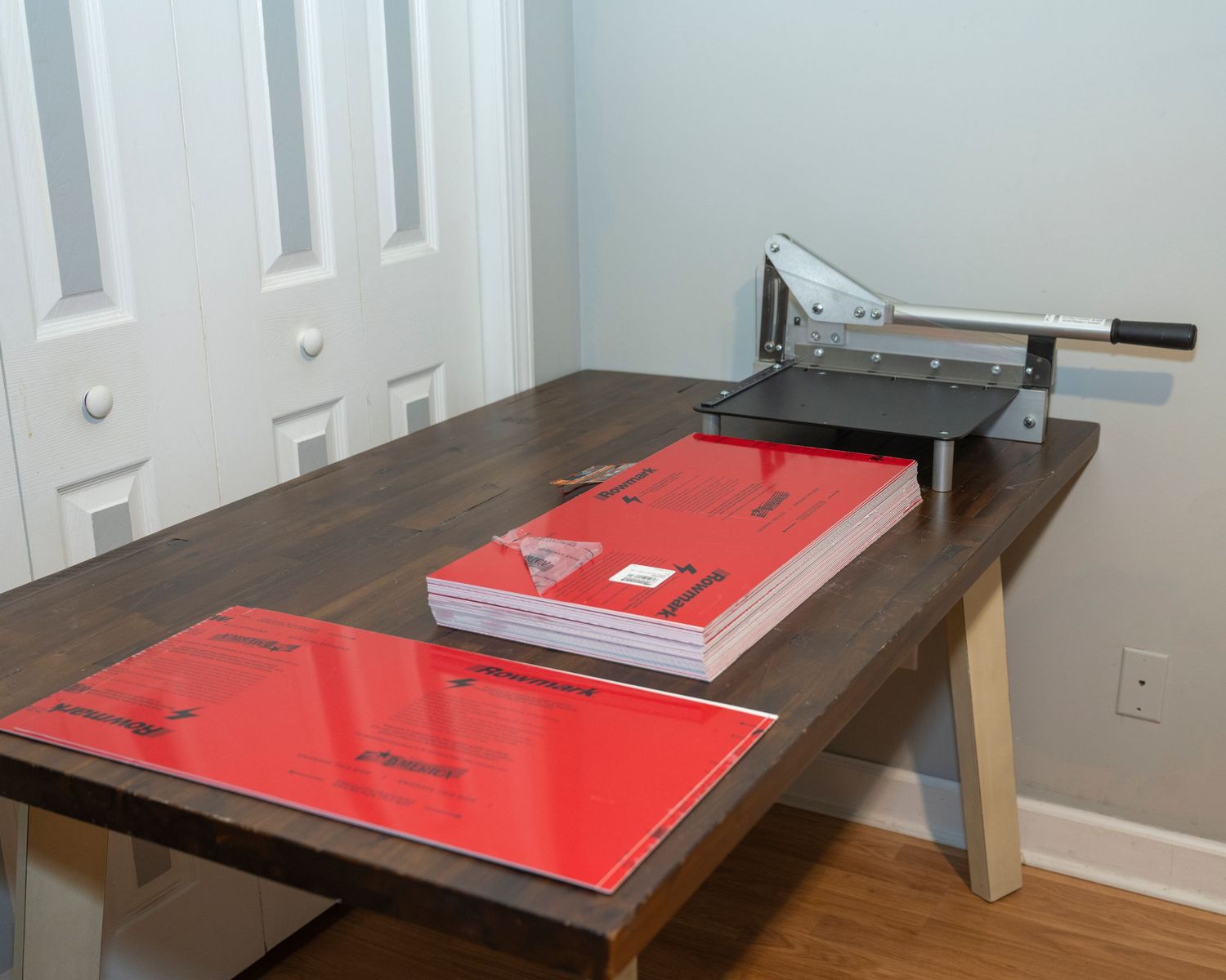Heavy-duty paper cutter guillotine trimmer on a dark wood desk with stacked red folders in a home office.