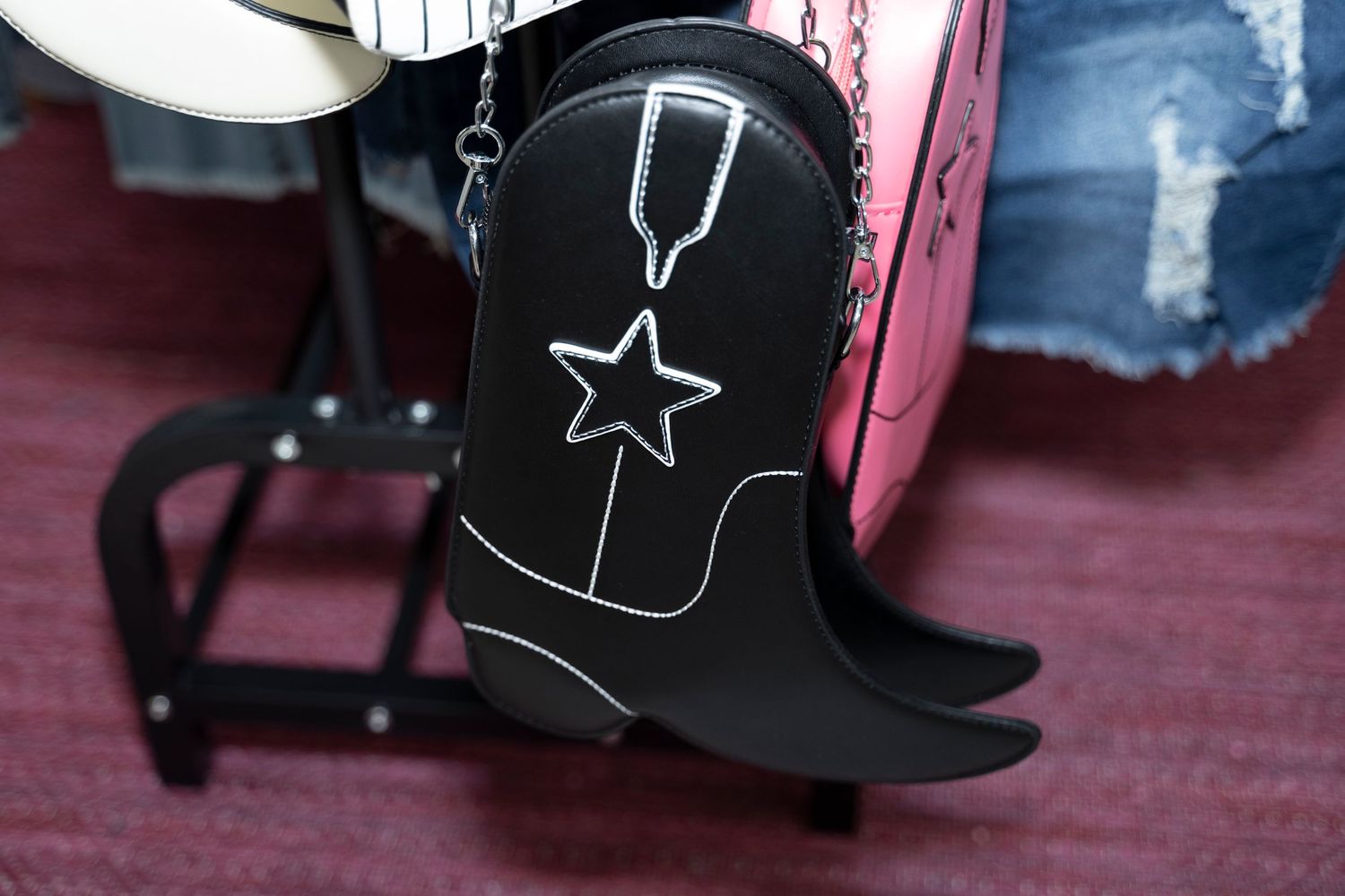Black cowboy boot with white star and stitching detail displayed against a pink background.