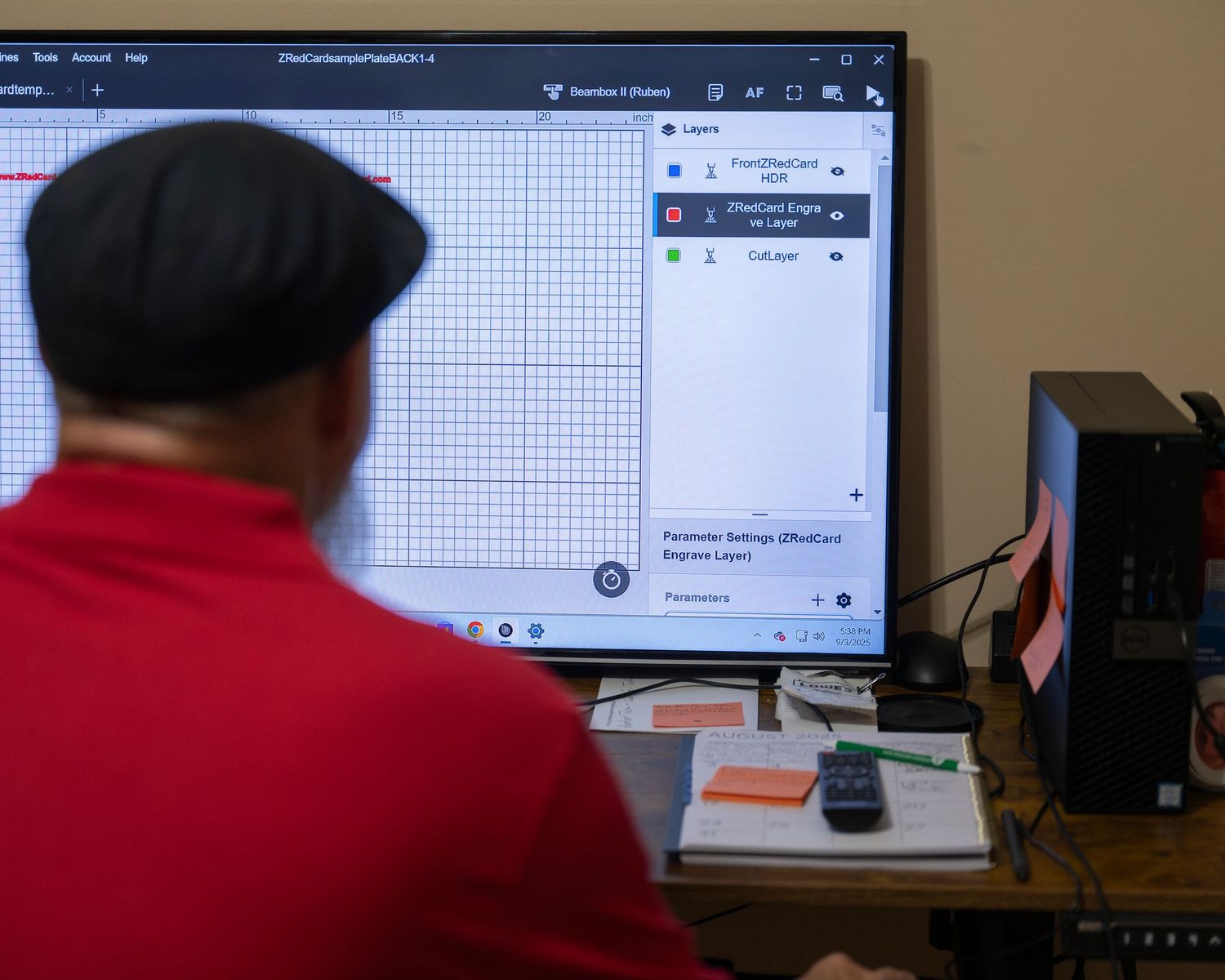 Person in red shirt working at desktop computer with design software open on large monitor in office.