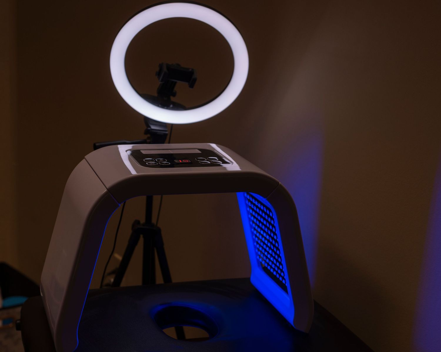 A glowing ring light mounted on a white photo booth with blue LED lighting in a dark room.