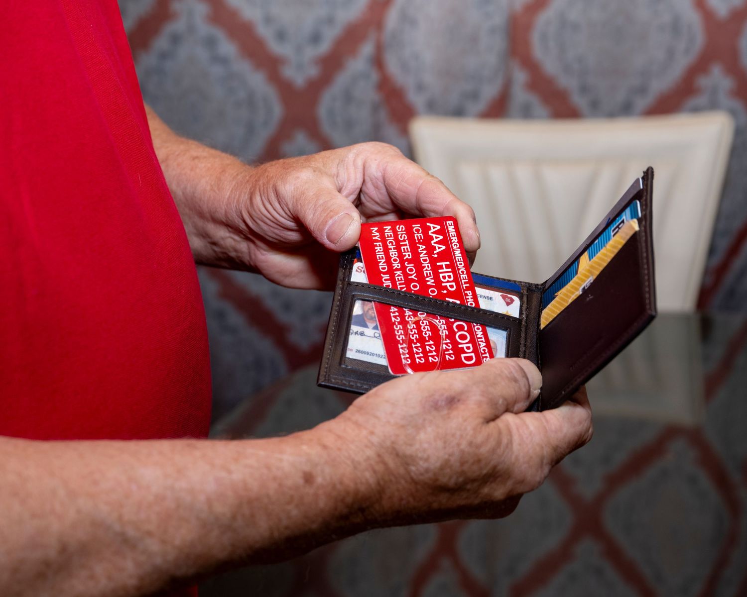 Elderly hands holding a brown leather wallet with red COVID medical alert cards and credit cards inside.