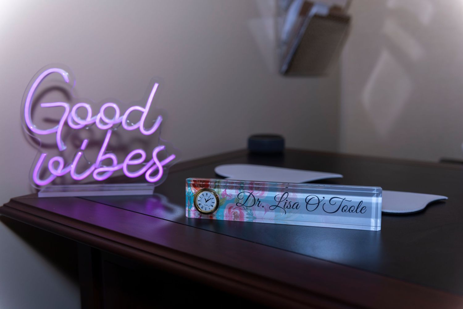 Desk with a pink neon 'Good Vibes' sign and a nameplate reading Dr. Lisa O'Toole in a modern office.