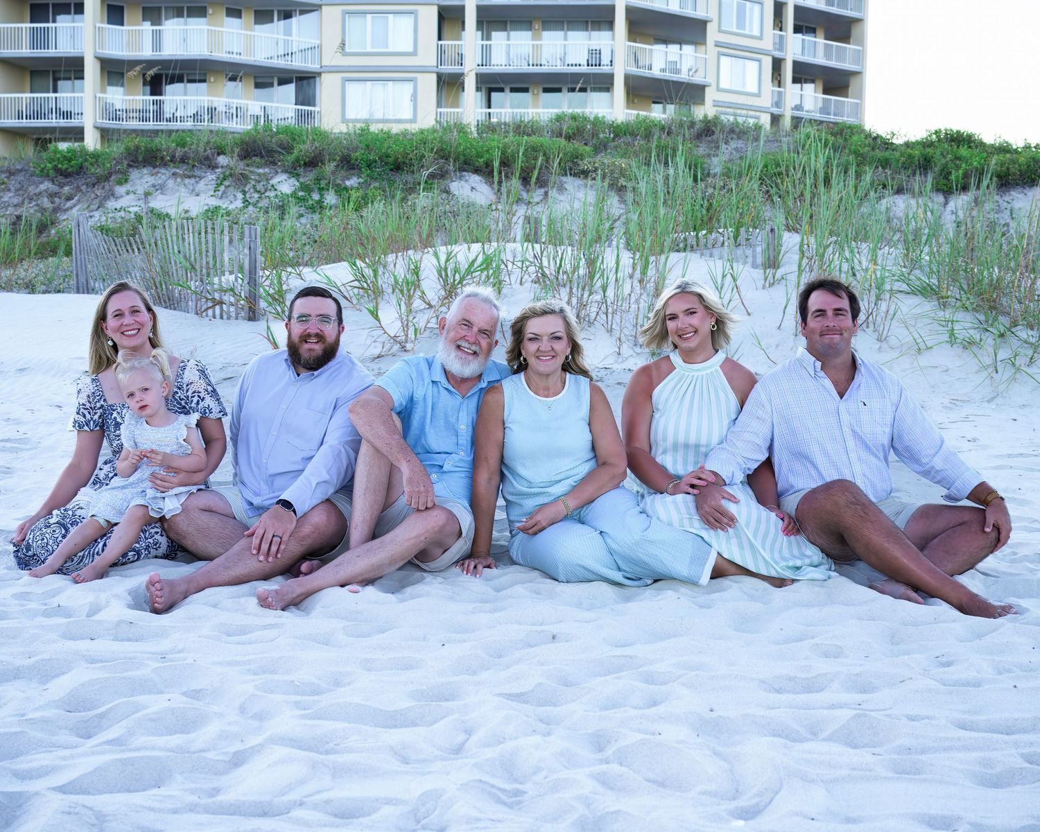 A group of people wearing white and blue outfits relaxing together on a sandy beach at sunset.