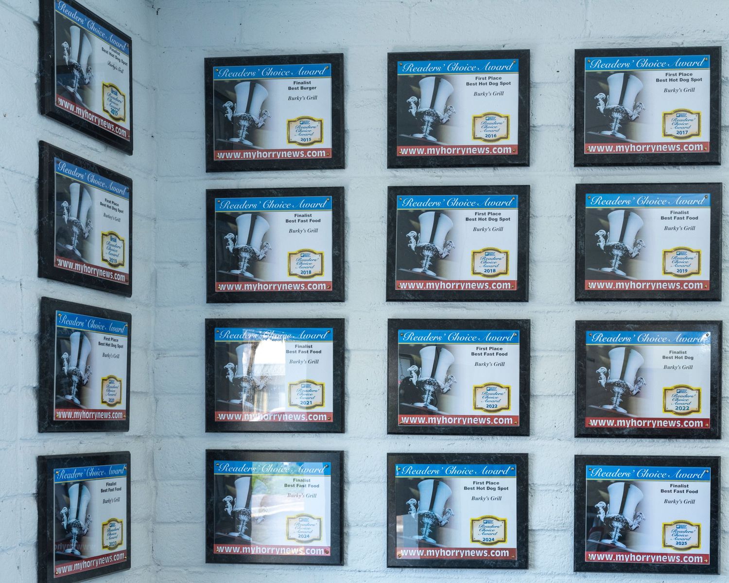 Wall display of 12 identical framed advertisement posters for a mixer product on a white brick wall.
