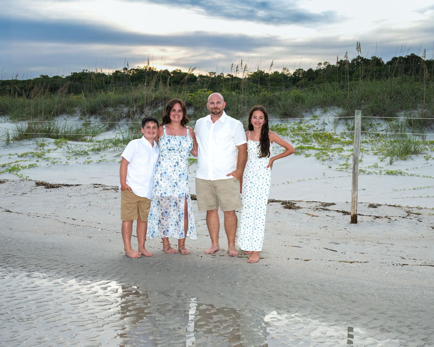 Family members stand together on a sandy beach at sunset wearing coordinated white outfits.