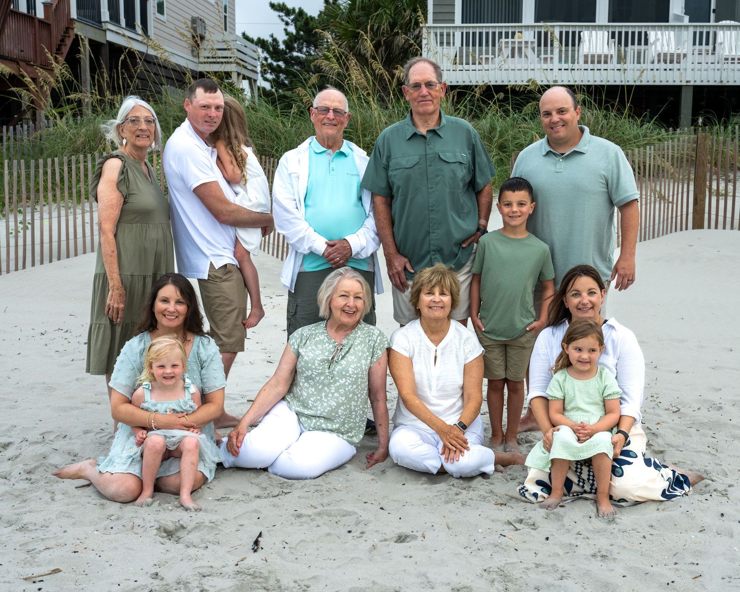 A group of people sitting together on a white sandy beach with a beach house visible in the background.