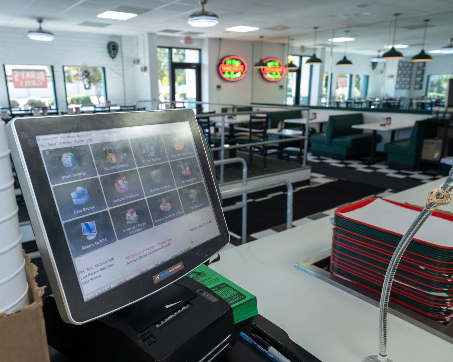 Modern POS touchscreen terminal at a diner restaurant counter with menu items displayed, booths visible in background.