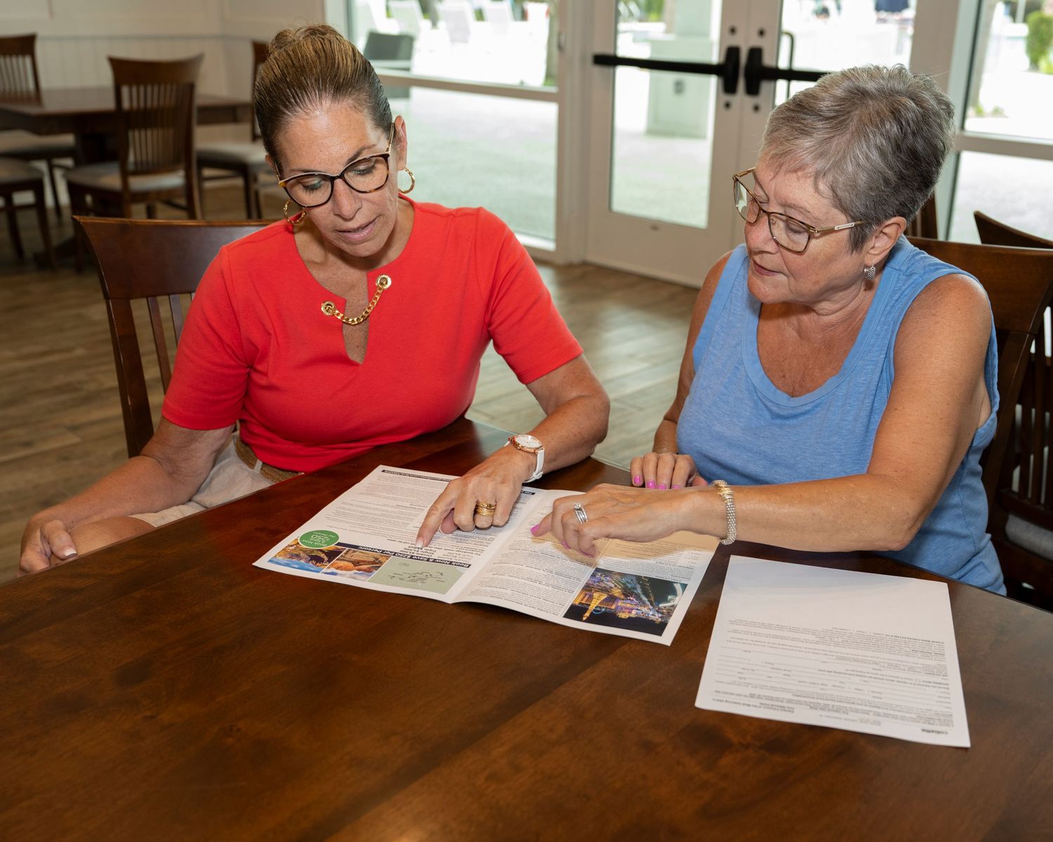 Two women reviewing a magazine together at a wooden table in a bright, casual dining setting.
