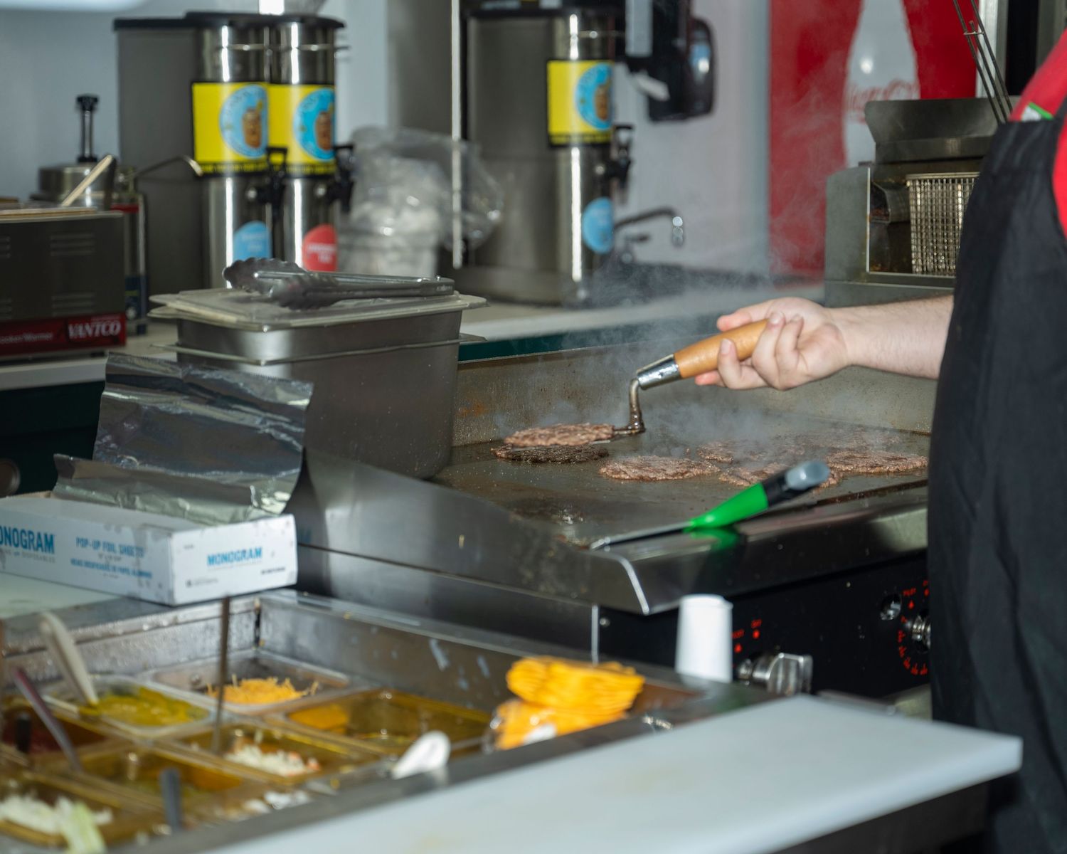 Cook grilling burger patties on a flat top griddle in a fast food restaurant kitchen.