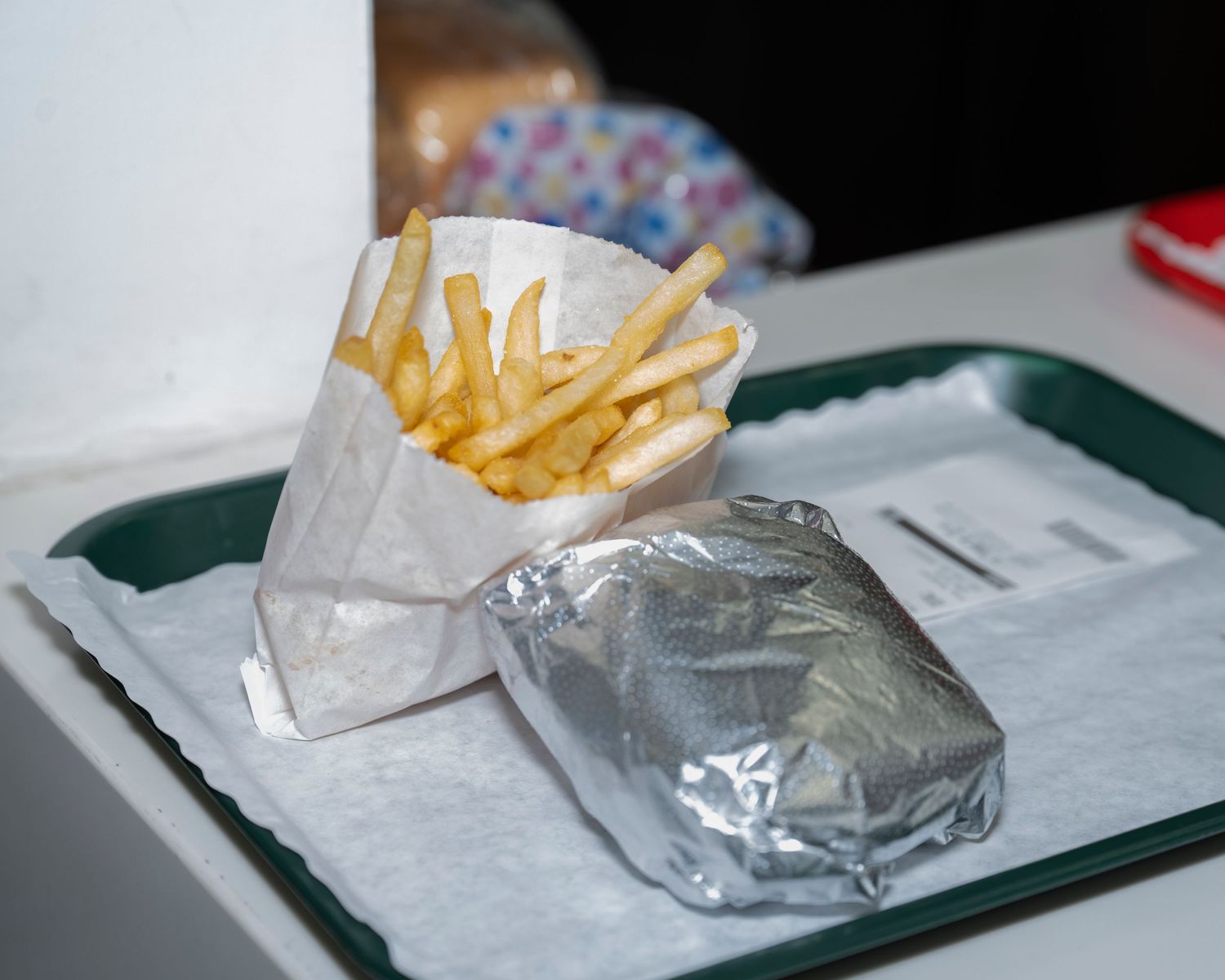 French fries in paper sleeve and foil-wrapped burger on a green fast food tray.