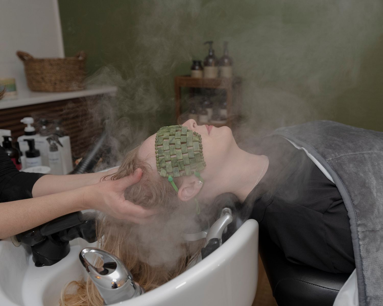 Person receiving a relaxing hair wash treatment at a salon with steam rising from the shampoo bowl.