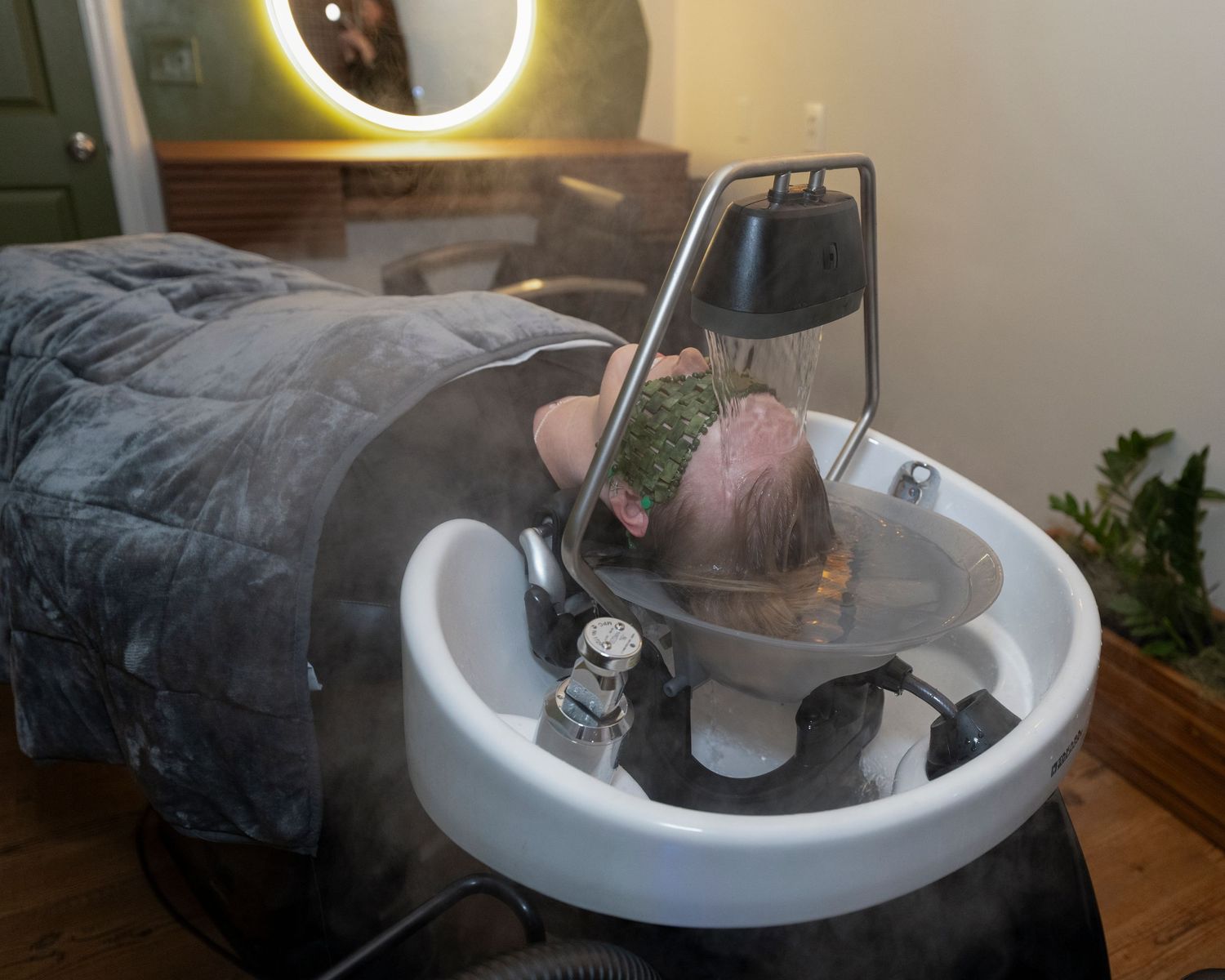 Person receiving a relaxing hair wash treatment at a salon shampoo bowl with steam and ambient lighting.
