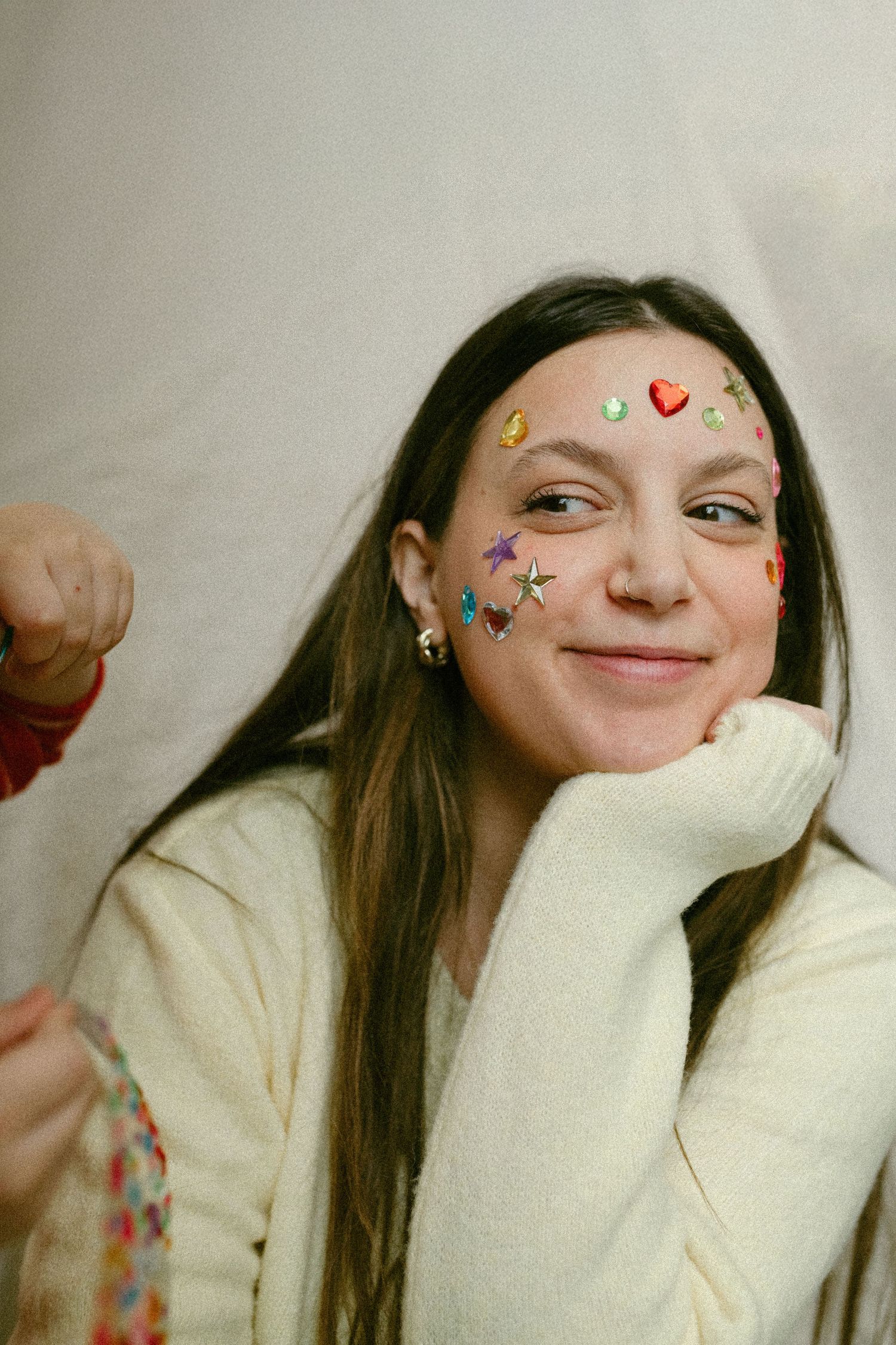 Person wearing a cream sweater with decorative face stickers of butterflies and hearts smiling at the camera.